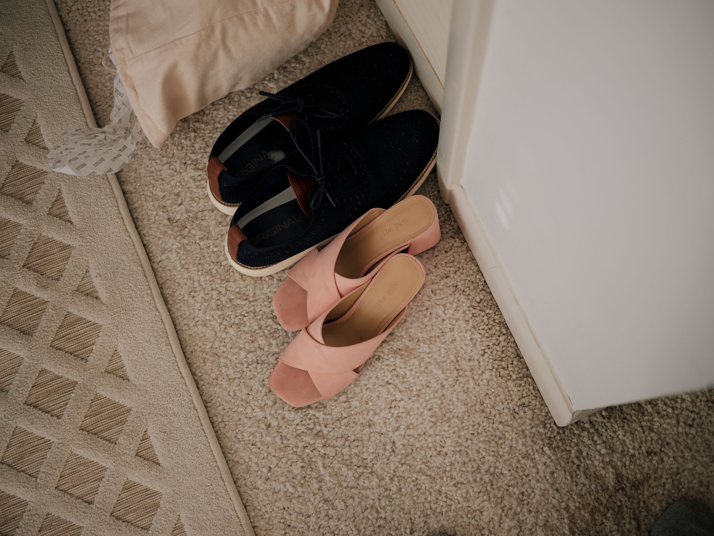 Wedding shoes lined up against a white wall on beige carpet.