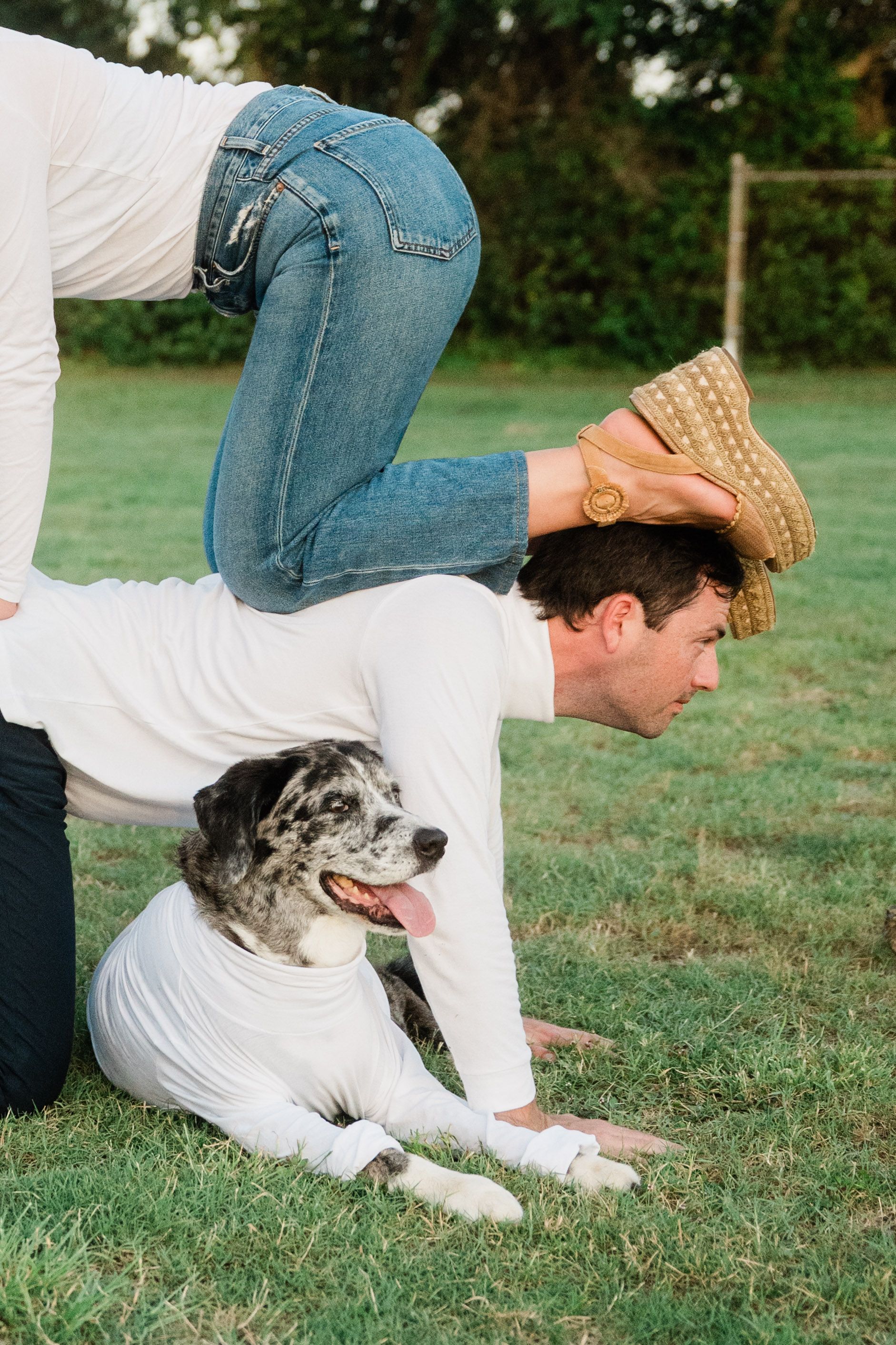 A black and white dog lies on grass next to someone wearing jeans and a white shirt in an outdoor setting.