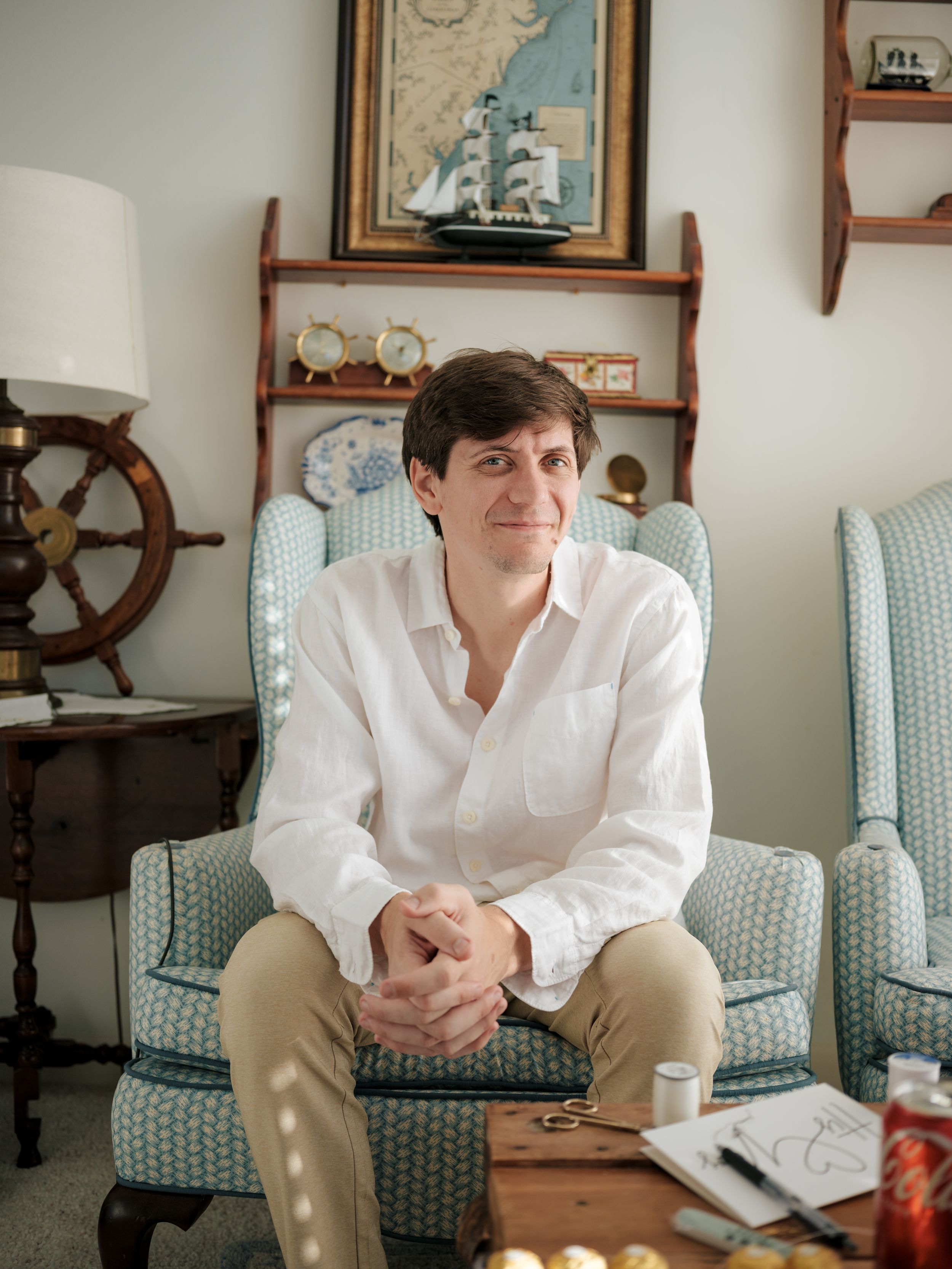 A person in a white shirt sits on a couch in a room decorated with nautical themed wall decor.