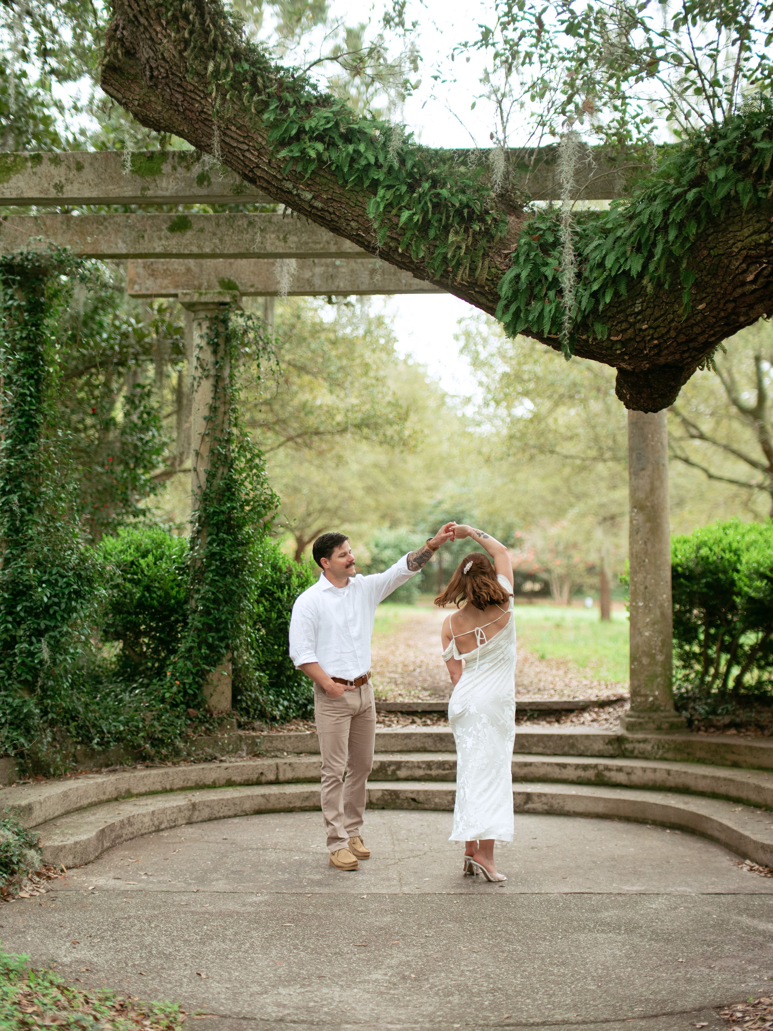 A couple dances together under a vine-covered pergola in a garden setting.