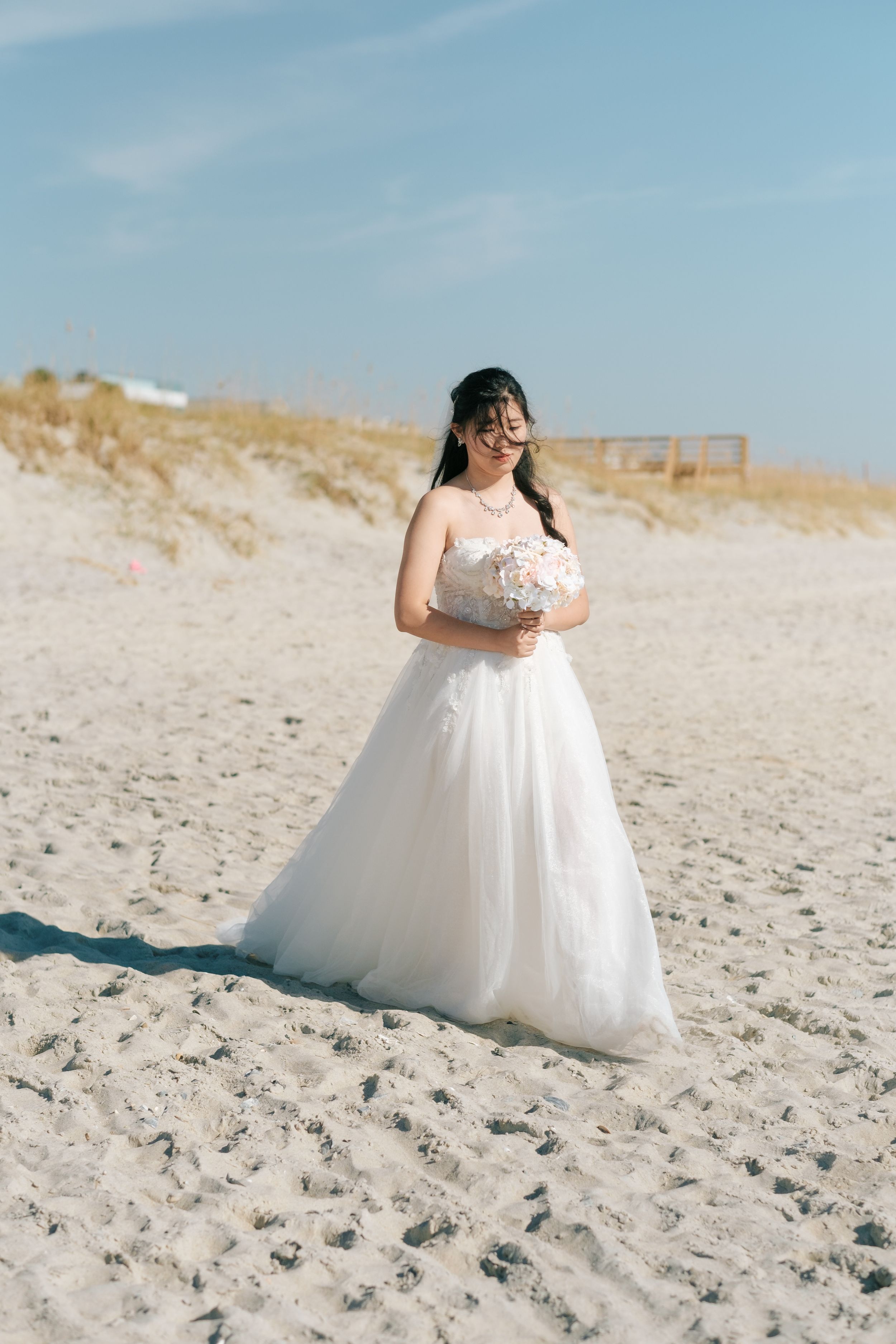A flowing white wedding dress spreads elegantly across golden beach sand.