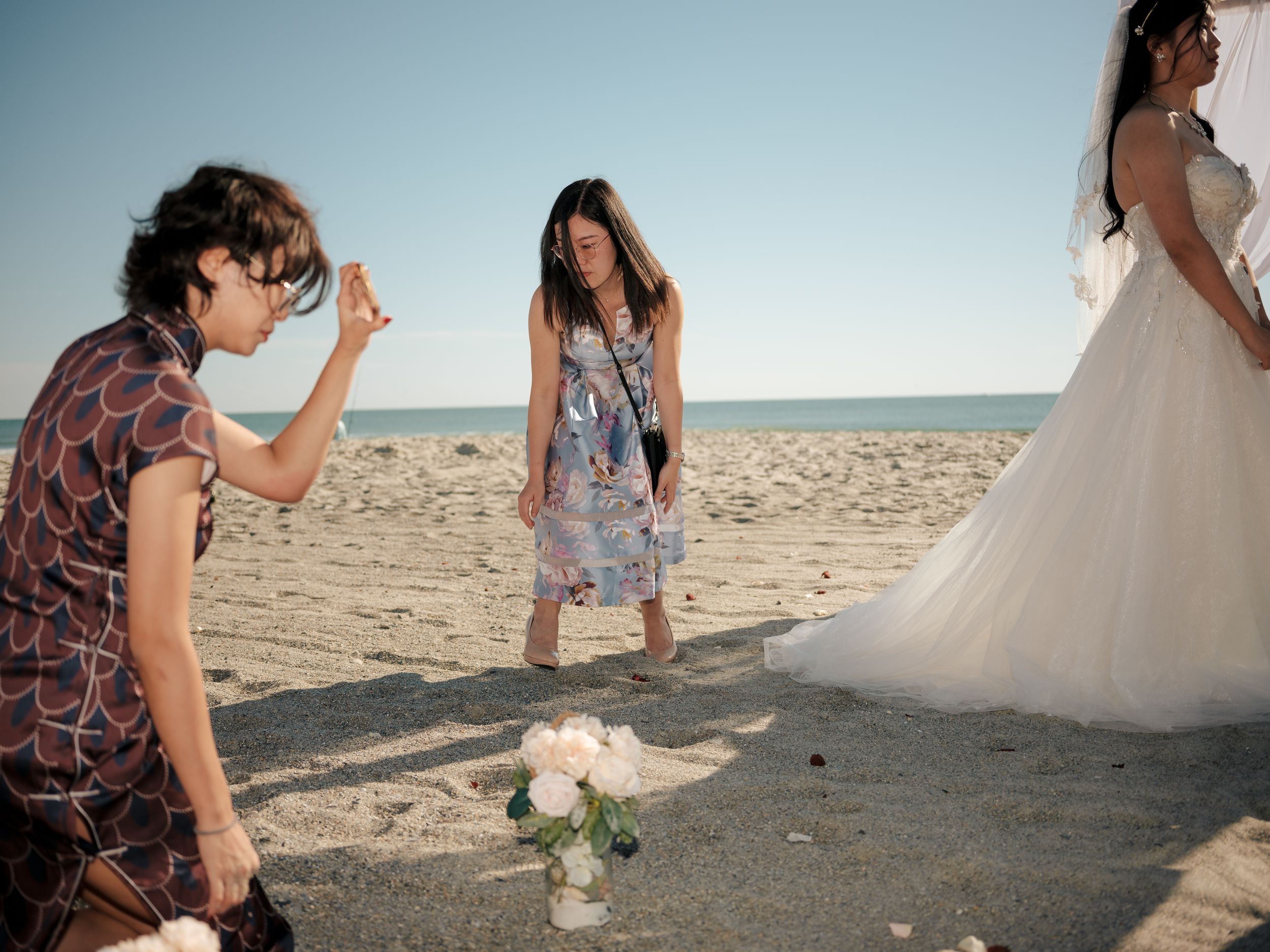 Wedding ceremony guests and bridal party gathered on sandy beach with ocean view.