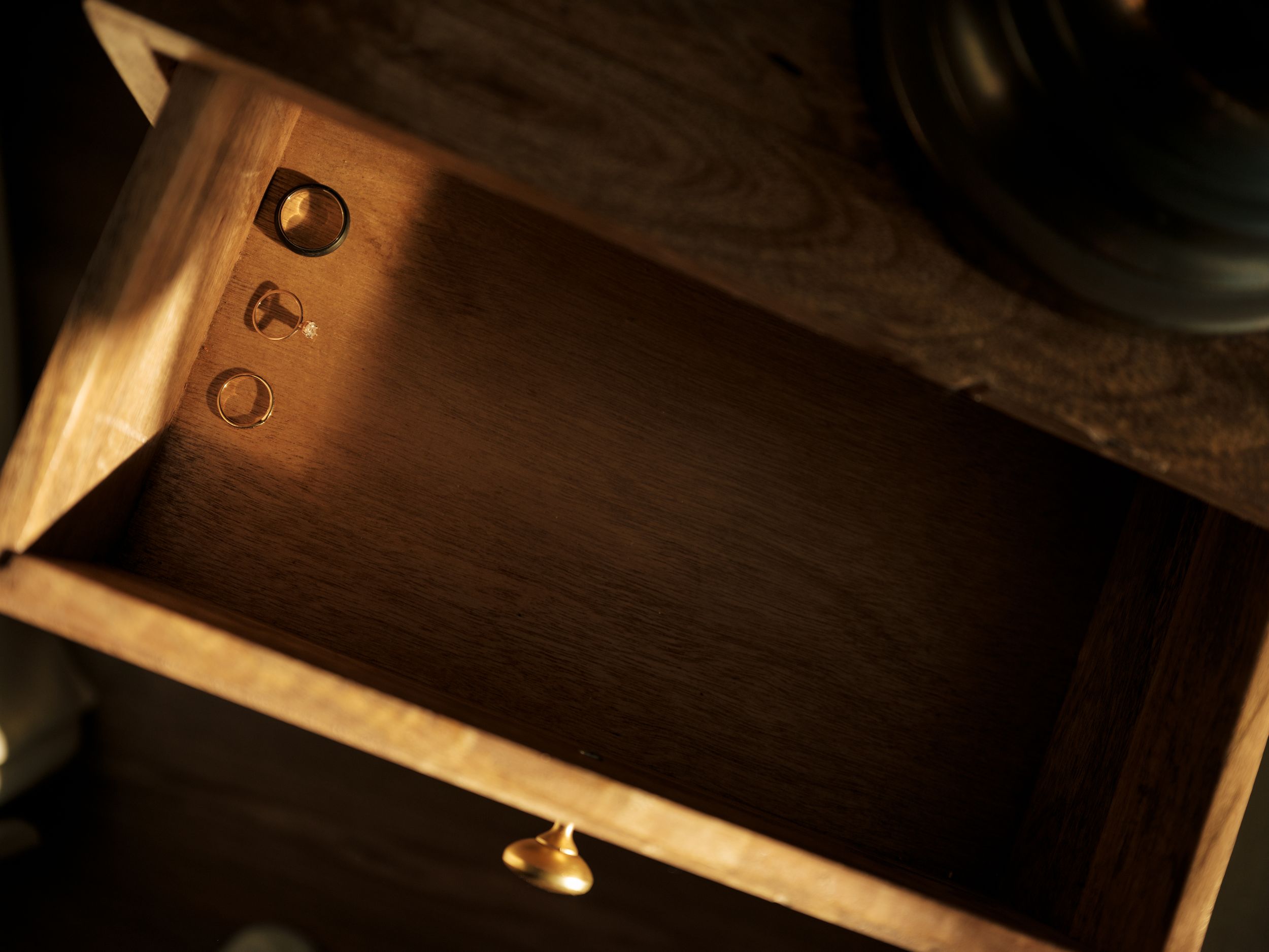 An open wooden drawer illuminated by warm light shows an empty interior and brass hardware details.