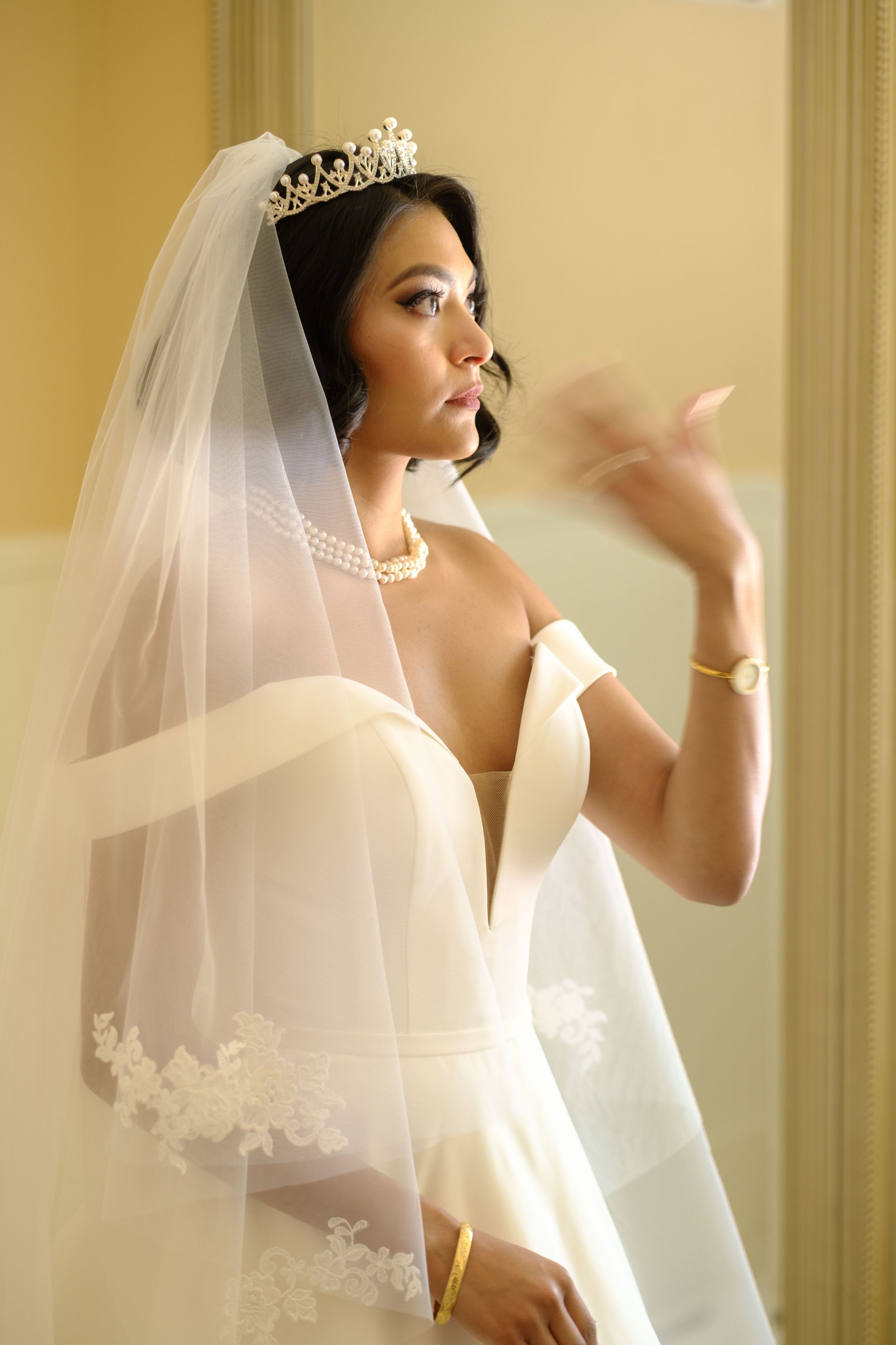 A bride in a white veil and crown appears in an elegant indoor setting with warm lighting.