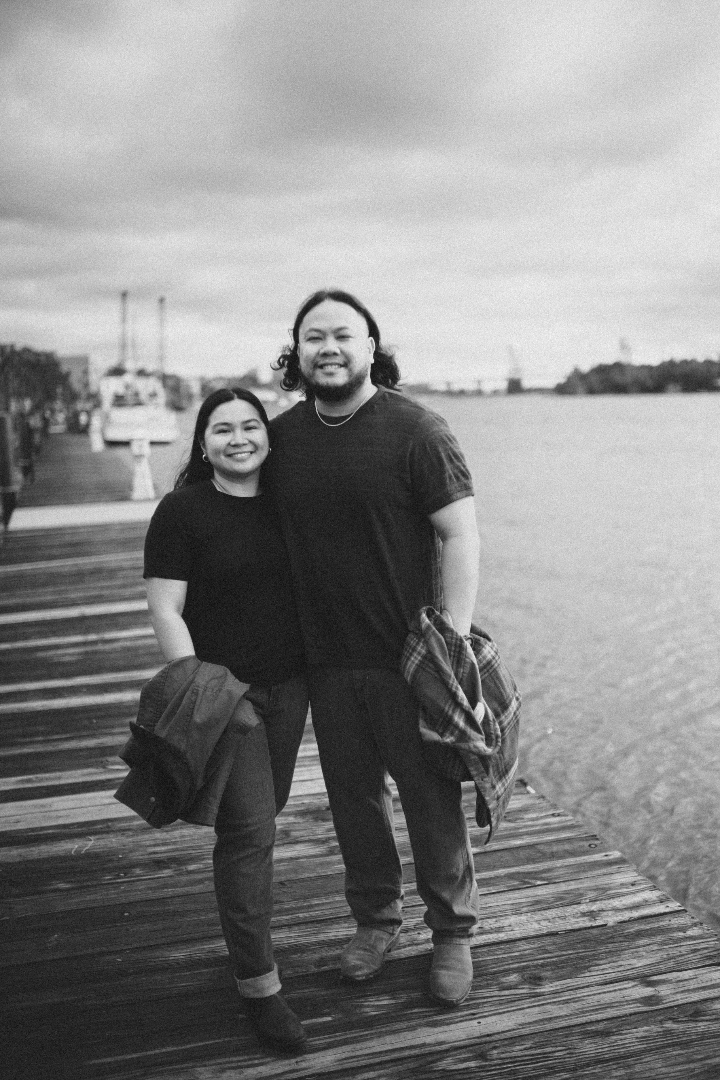 Black and white images of a couple sharing joyful moments on a wooden boardwalk by the water.