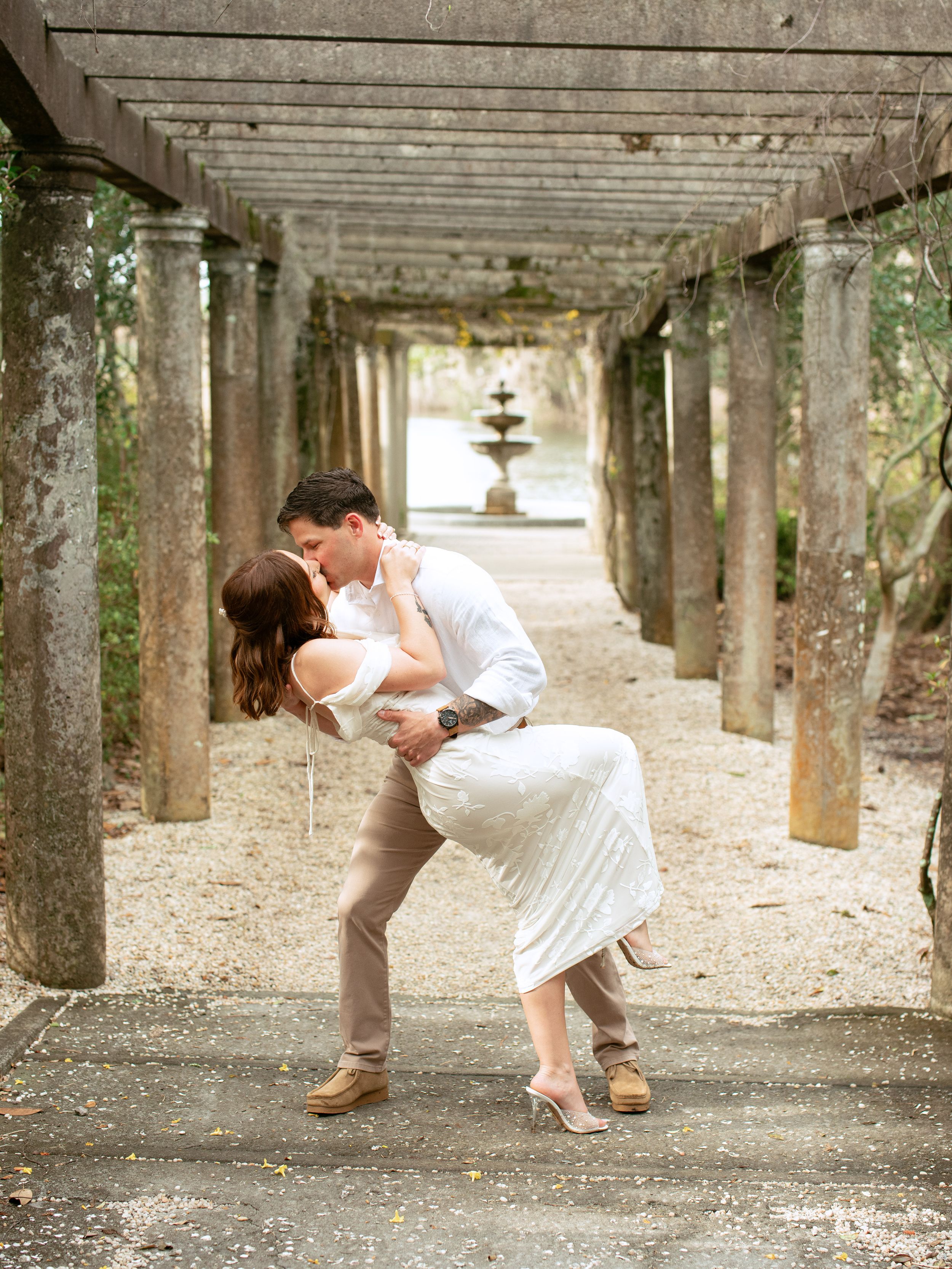 A romantic couple dips and embraces beneath a covered walkway lined with concrete pillars in a sequence of dance poses.