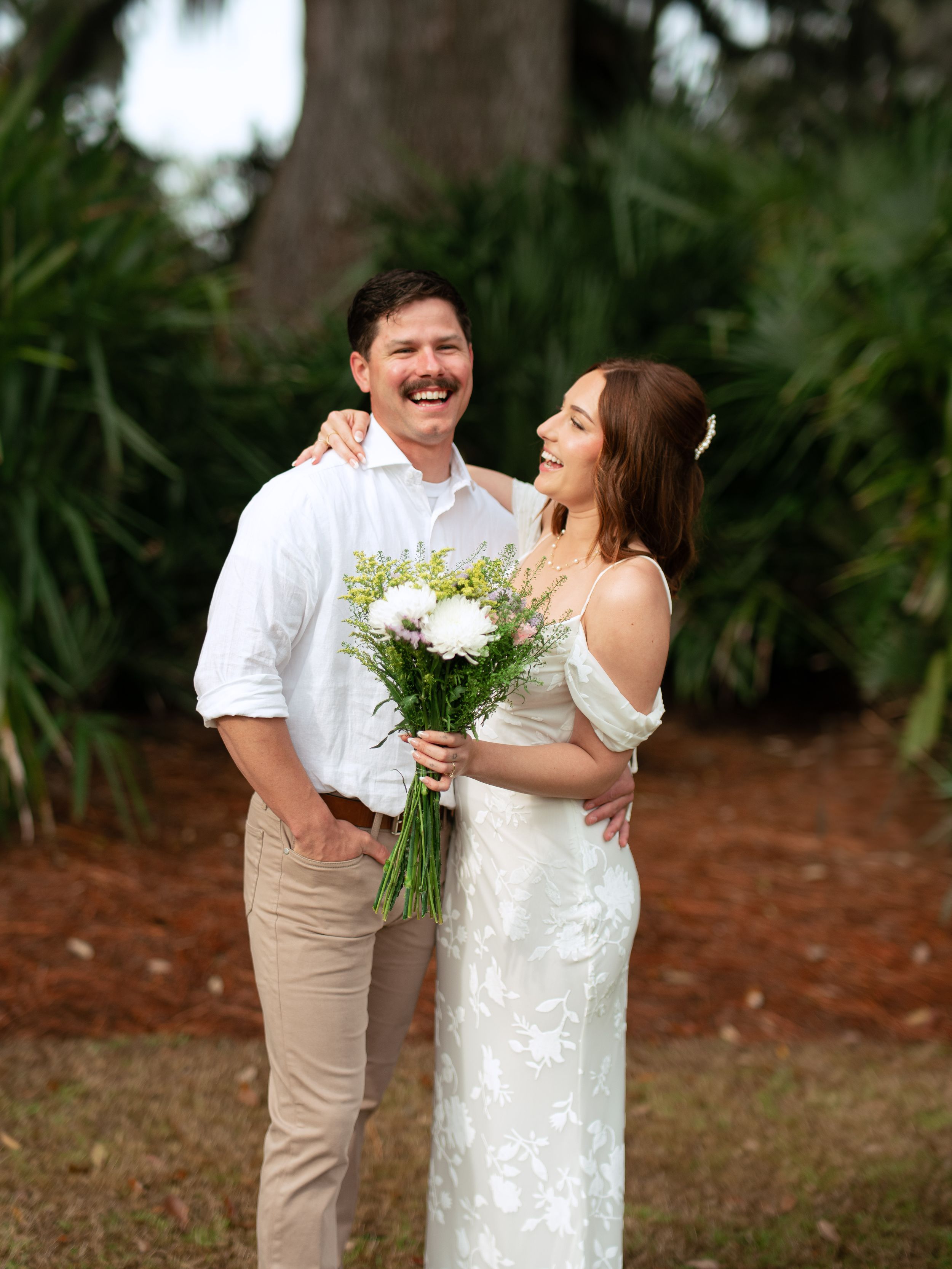 A couple in wedding attire share joyful laughs while embracing outdoors during their photo session.