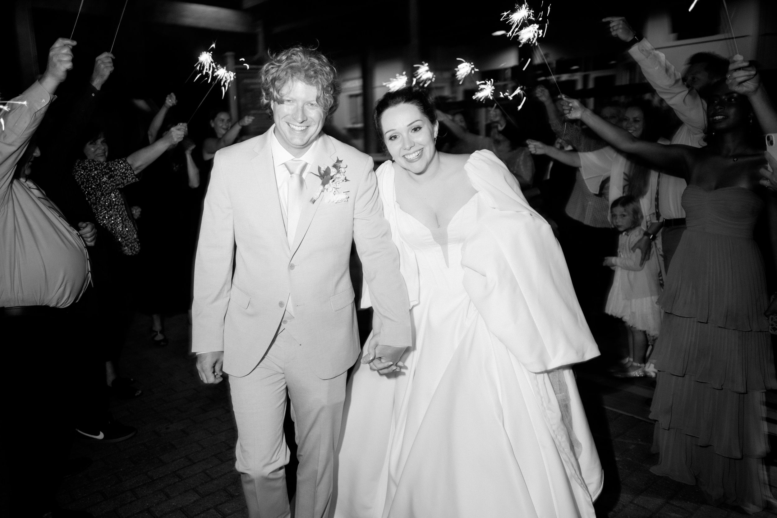 Wedding exit celebration with sparklers as couple walks through crowd at night.