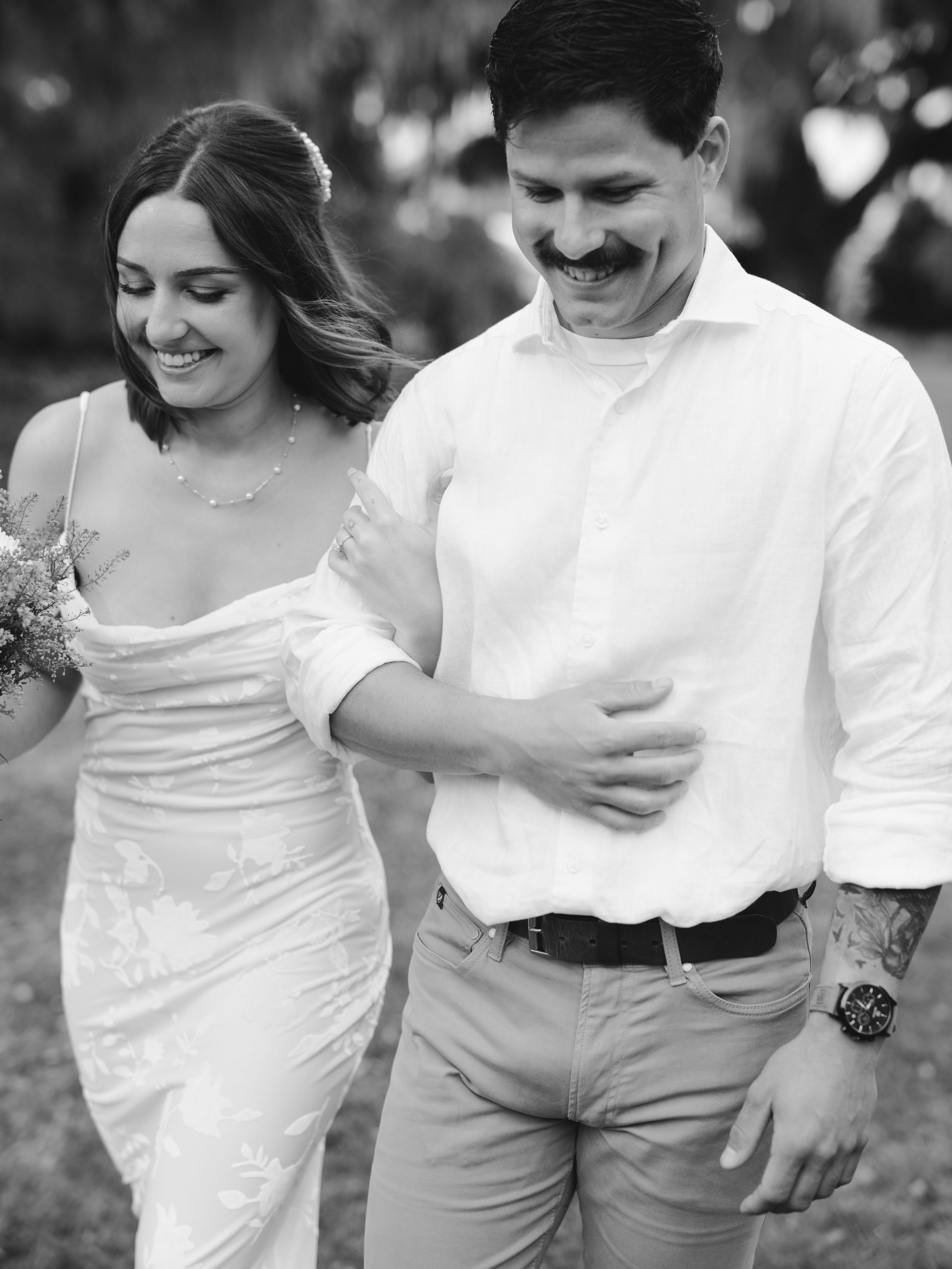 A couple dressed in white clothing laughs together while walking outdoors.