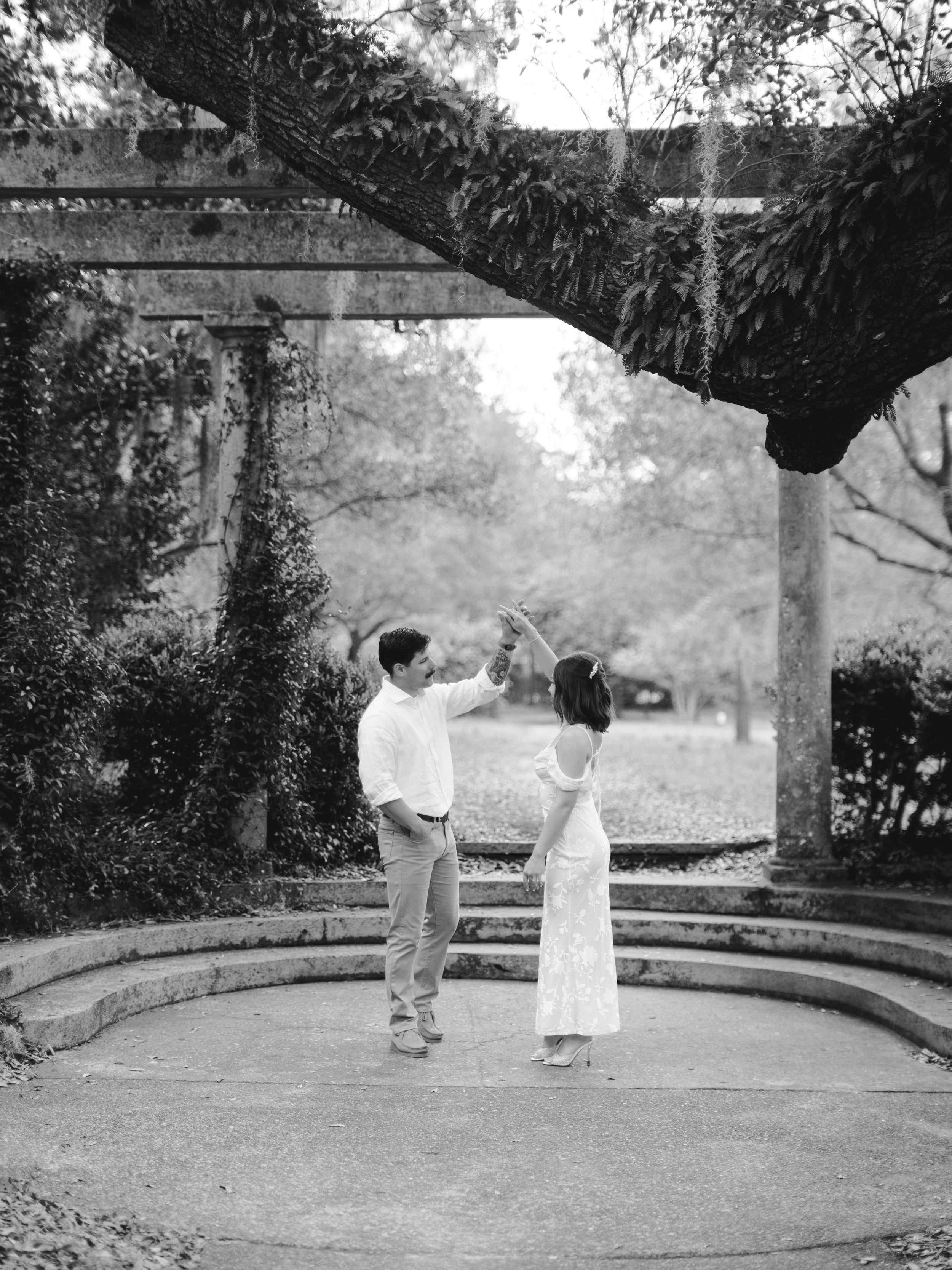 A black and white photo shows a couple dancing in a circular garden pergola.