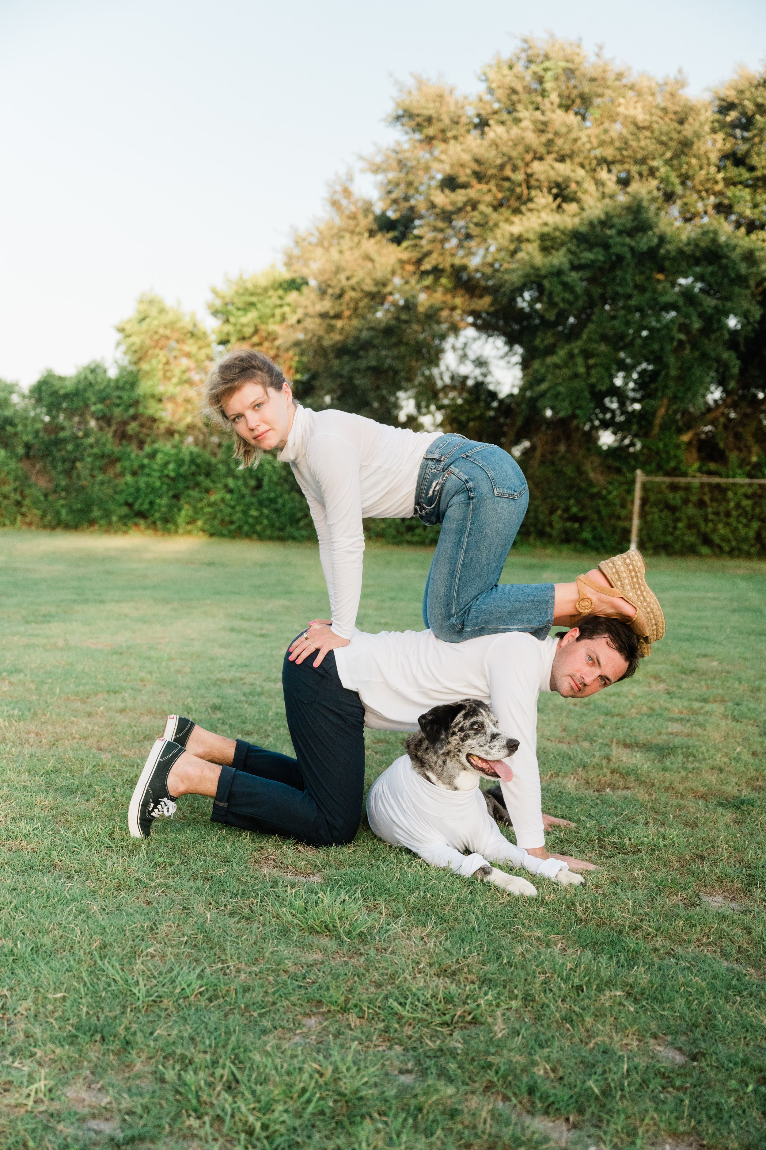 Person playfully rolling on grass with their dog in a park with trees in the background.