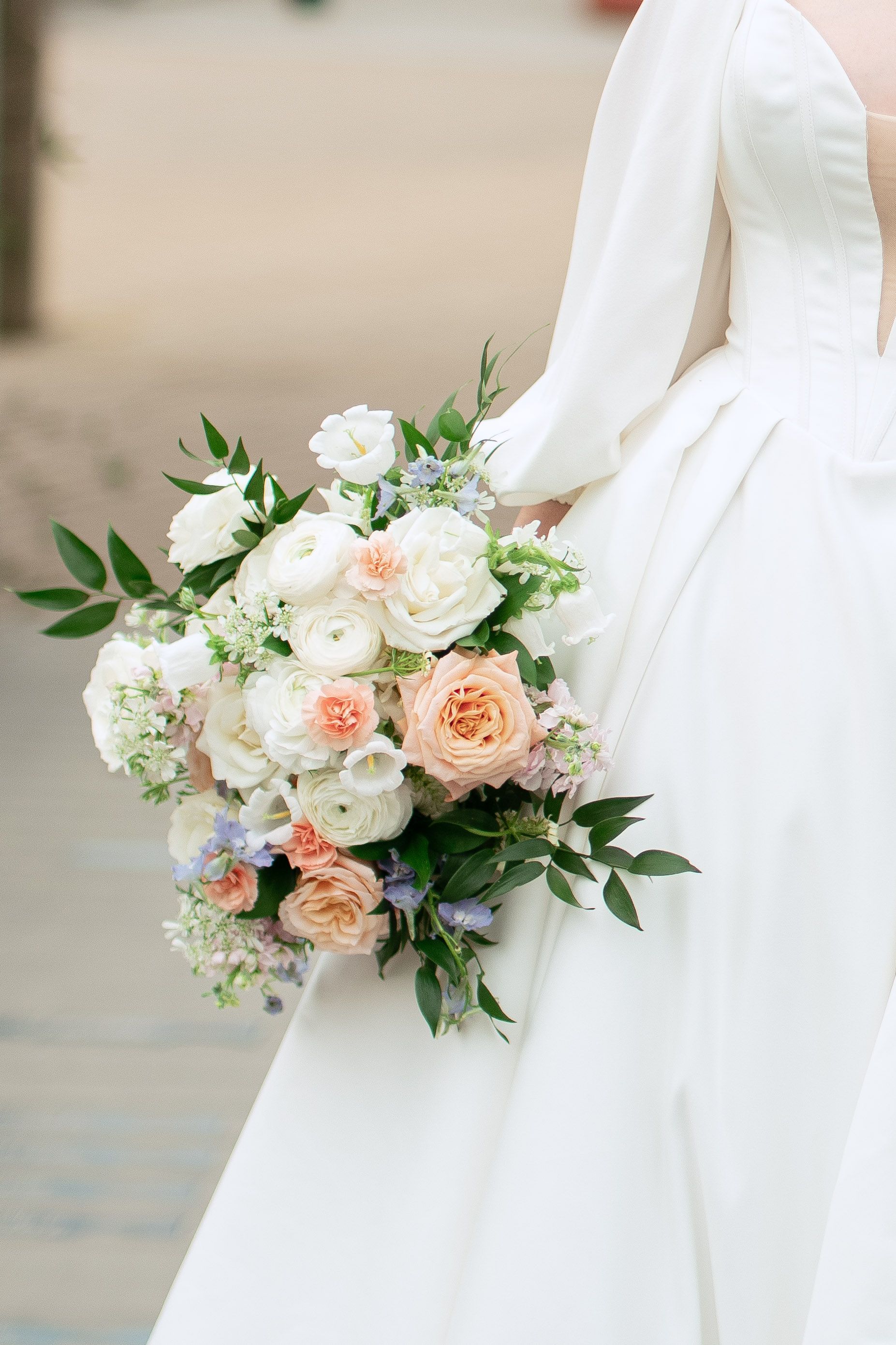 Delicate peach and white roses with greenery in a bridal bouquet against white fabric.