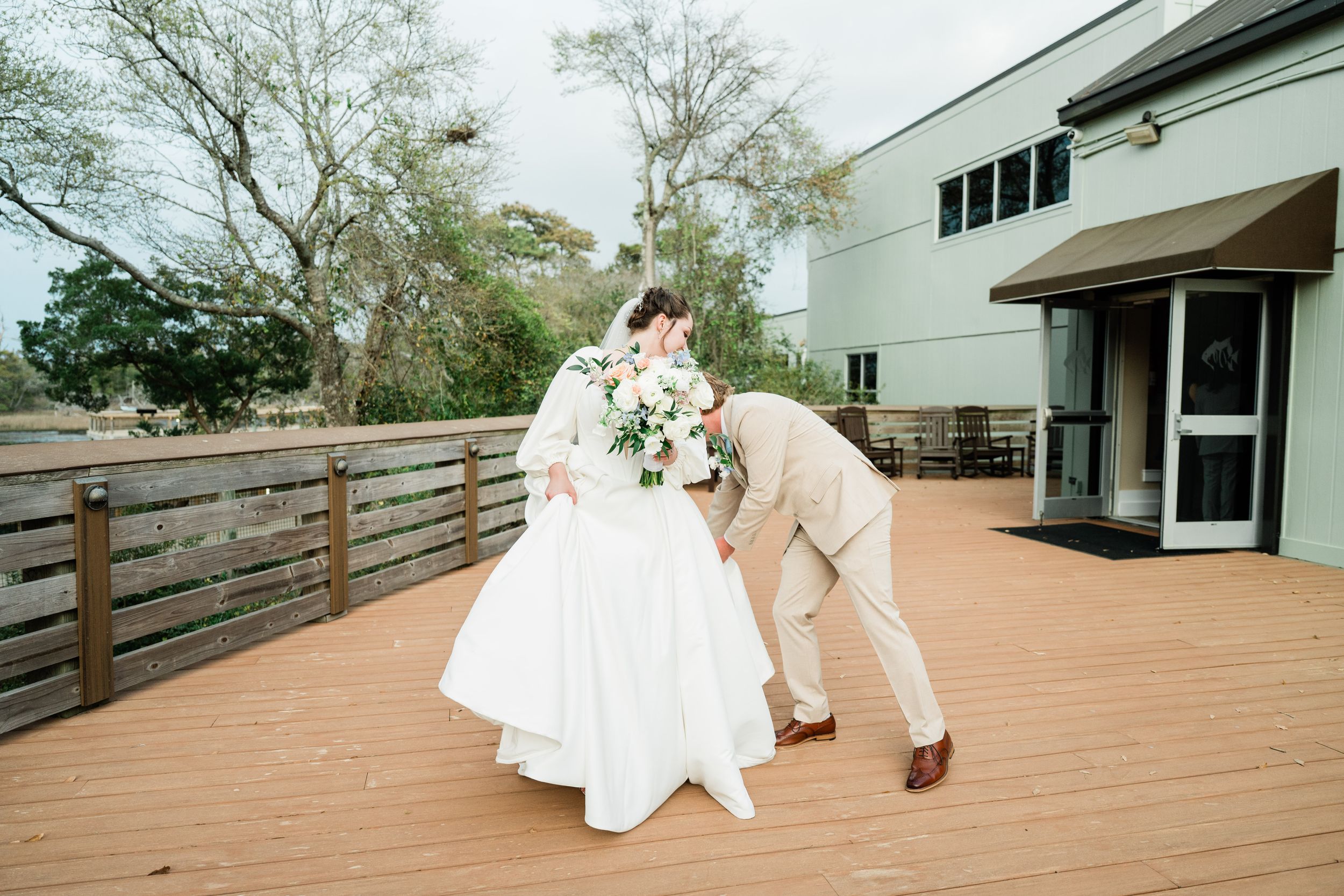 Couple shares playful moment on outdoor wooden deck during wedding celebration.