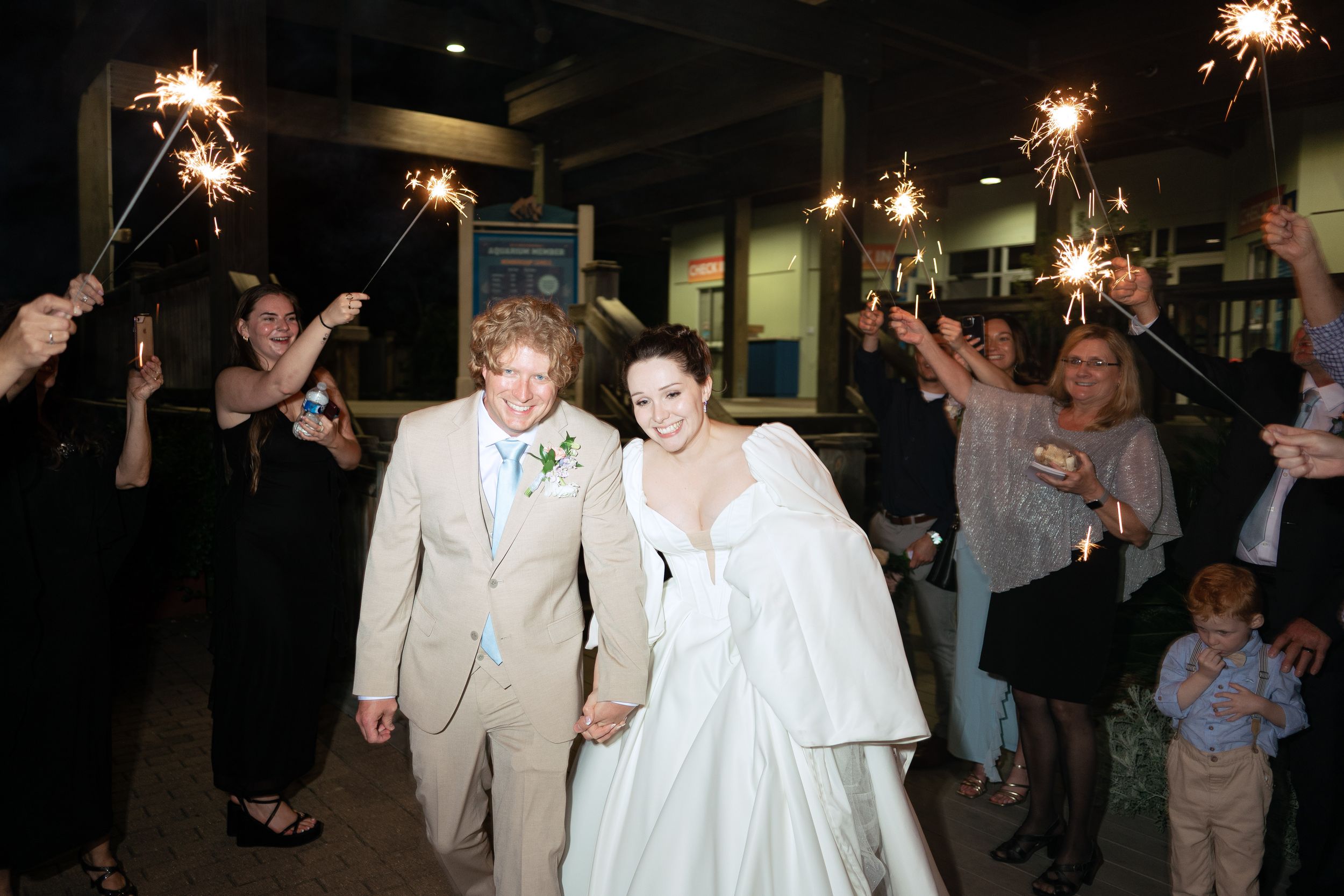 A couple walks through sparklers held by wedding guests during their evening celebration exit.