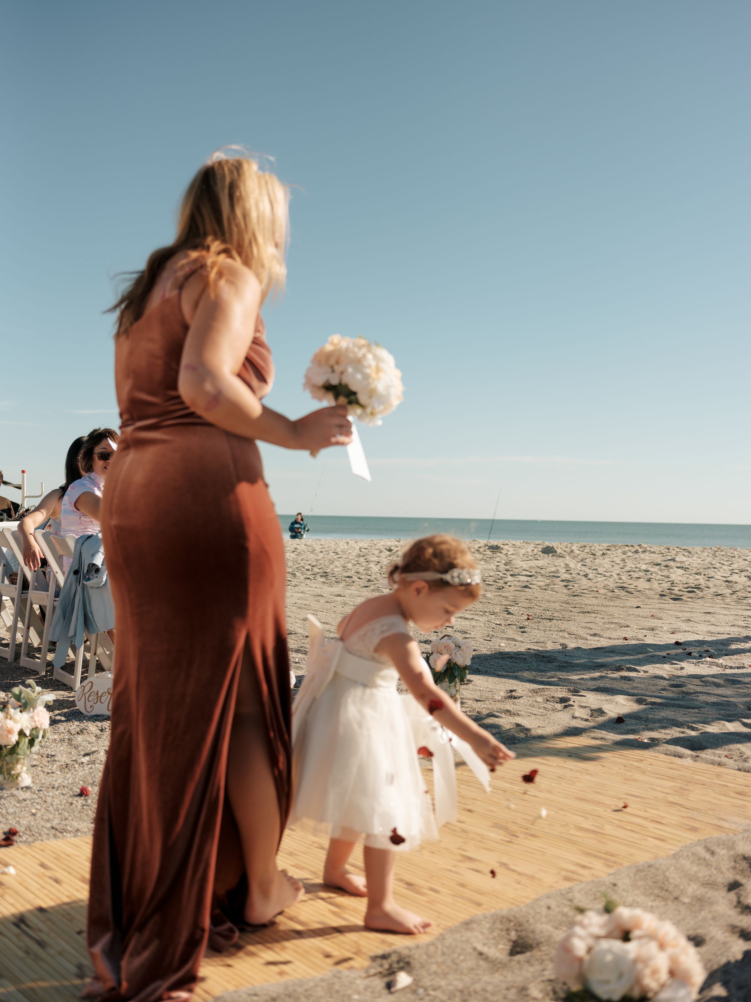 Beachside gathering with attendees sitting on sand watching an oceanfront event.