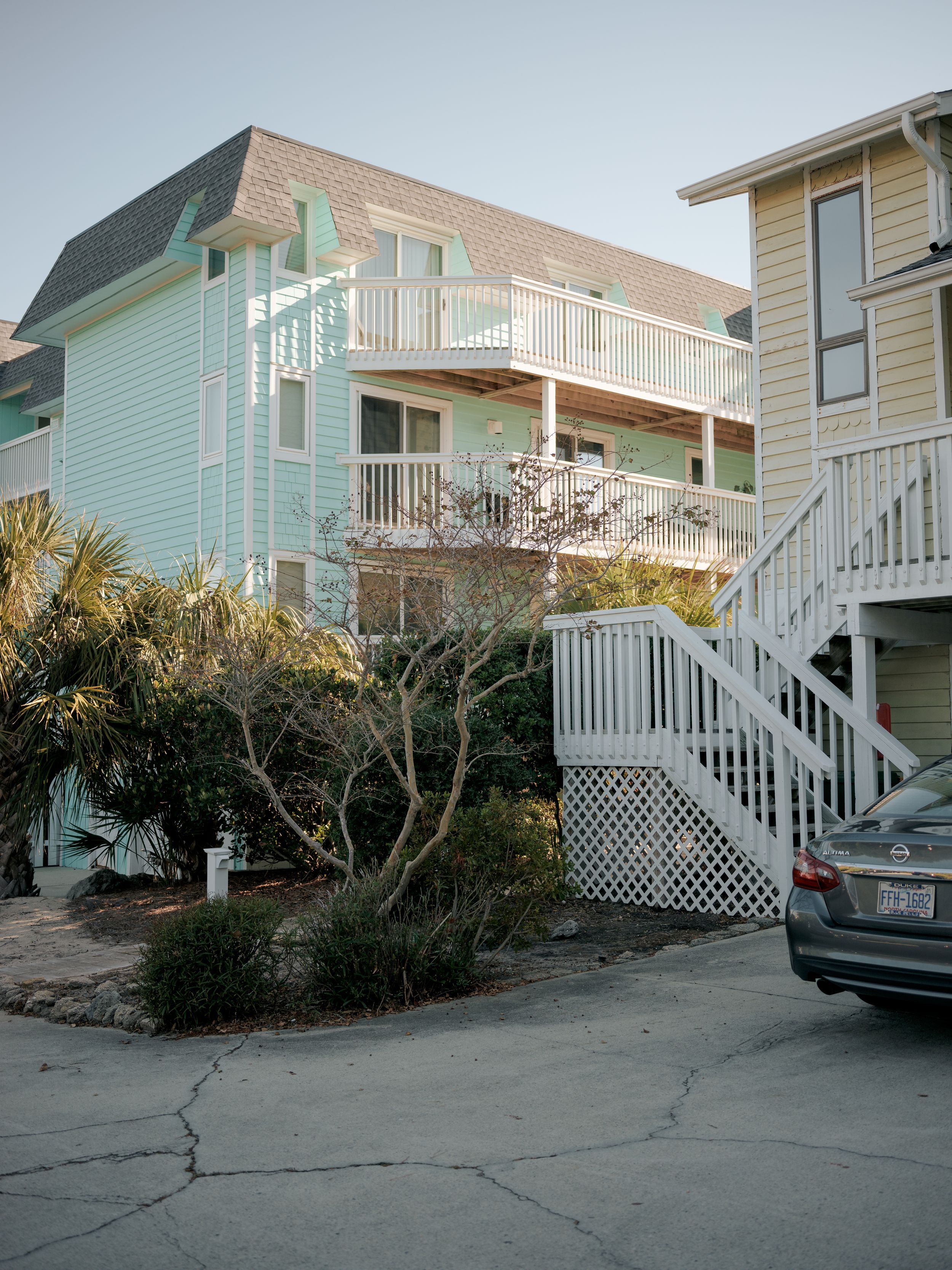 Pastel-colored beach house with multiple decks and white stairs in coastal setting.