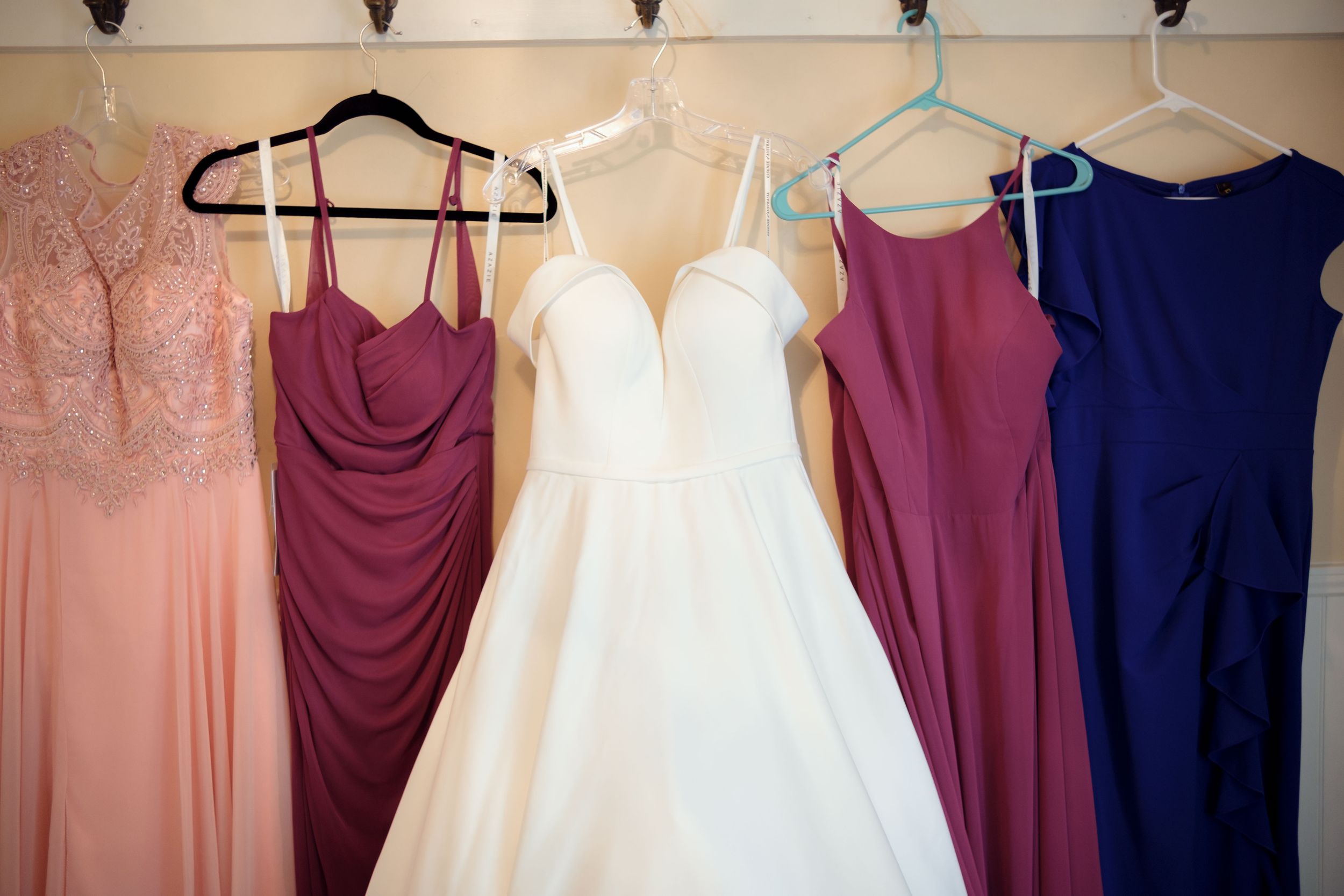 Wedding dresses and bridesmaid gowns in burgundy, navy, and blush pink hang on display.