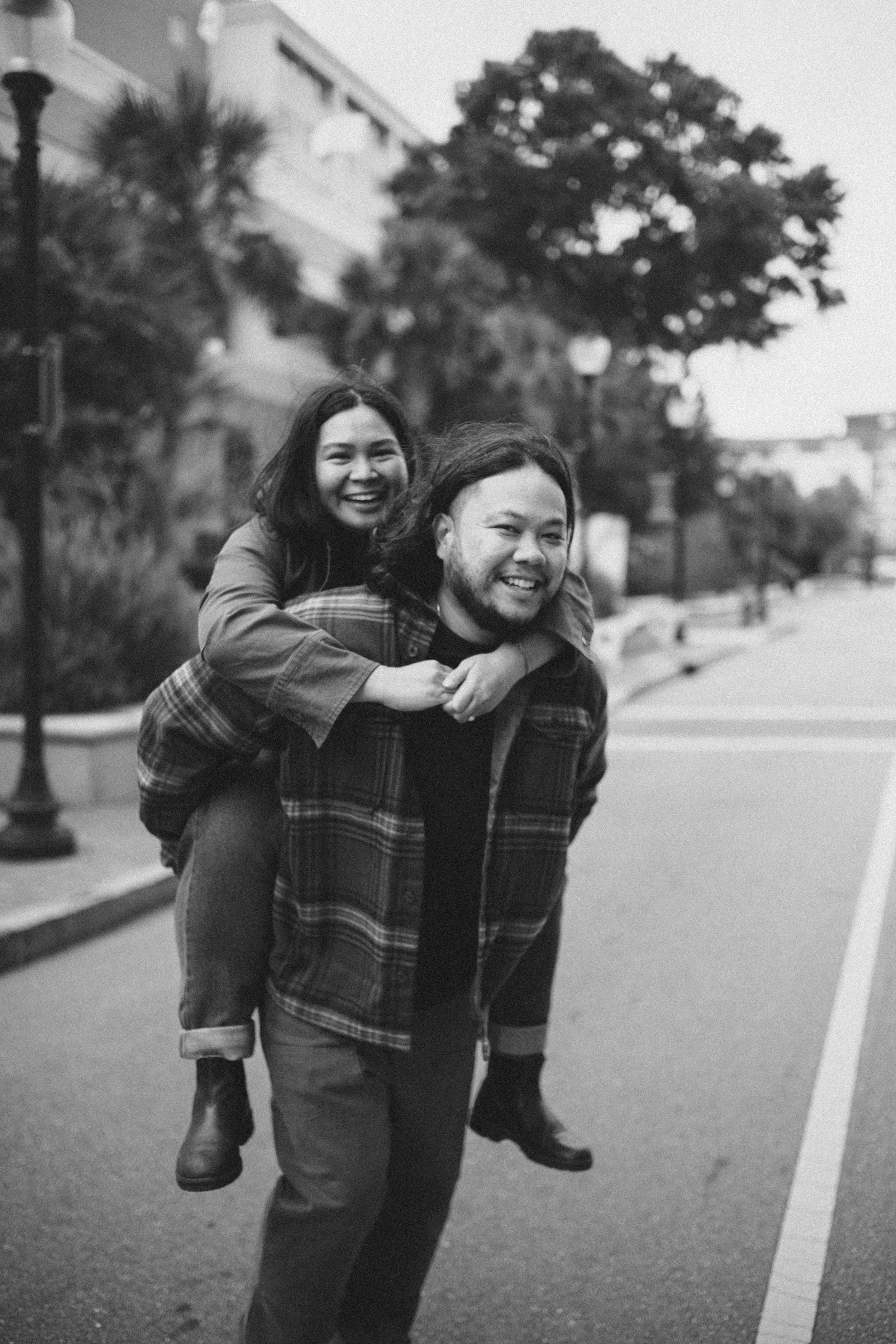 A playful piggyback ride moment captured in black and white on a suburban street.
