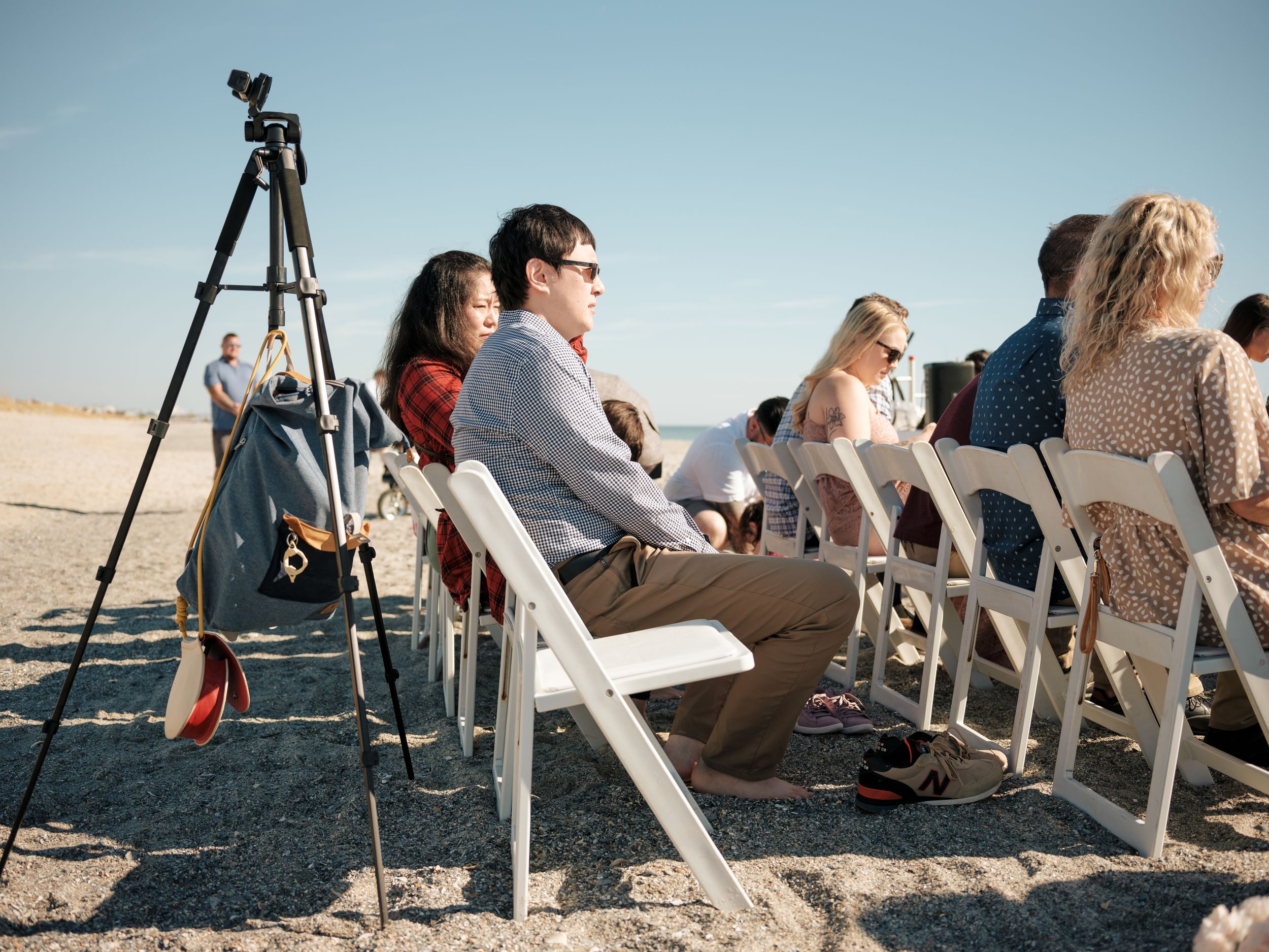 Wedding guests seated in white chairs on a beach during an outdoor ceremony.