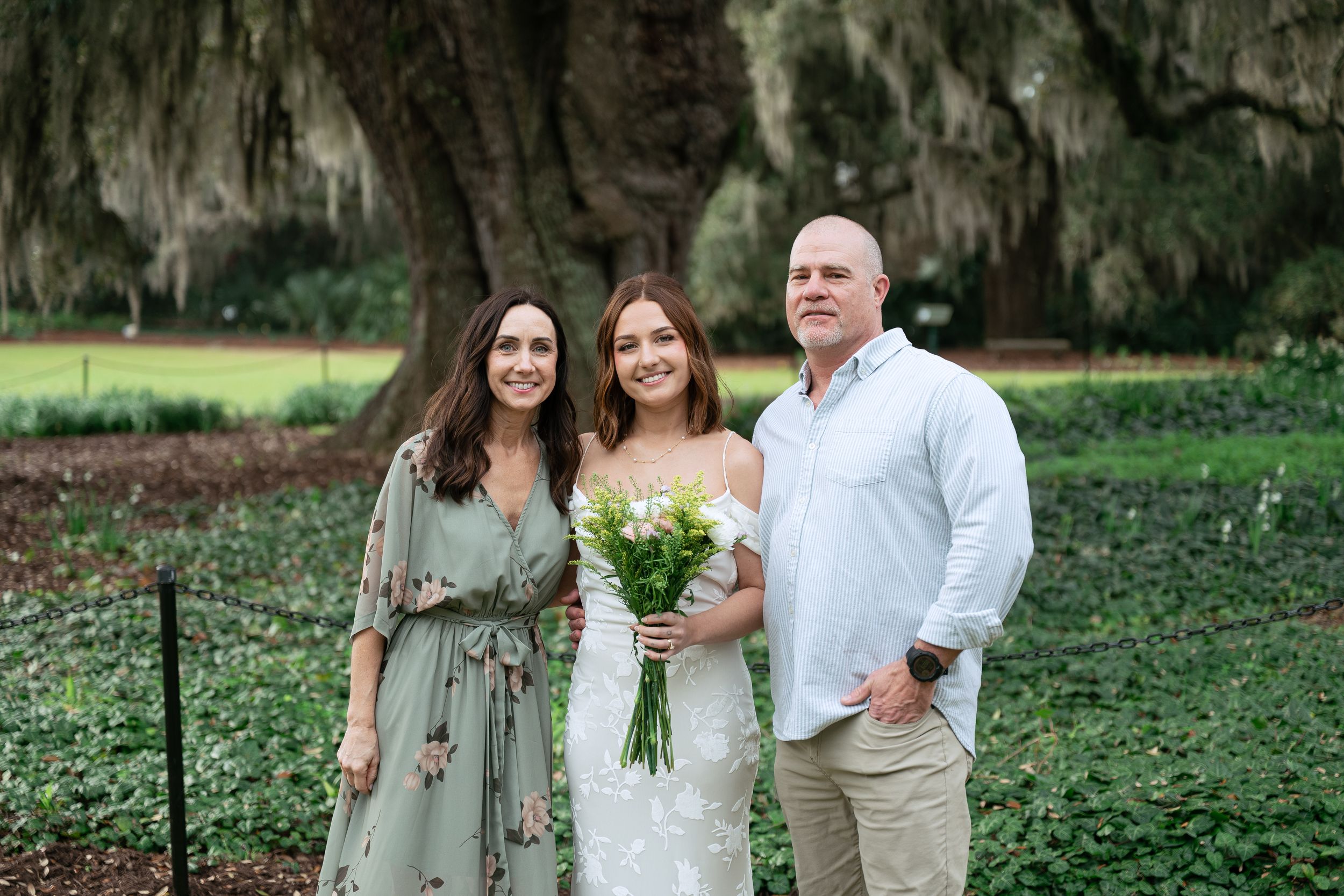People in coordinating green and white outfits pose together outdoors near hanging Spanish moss.
