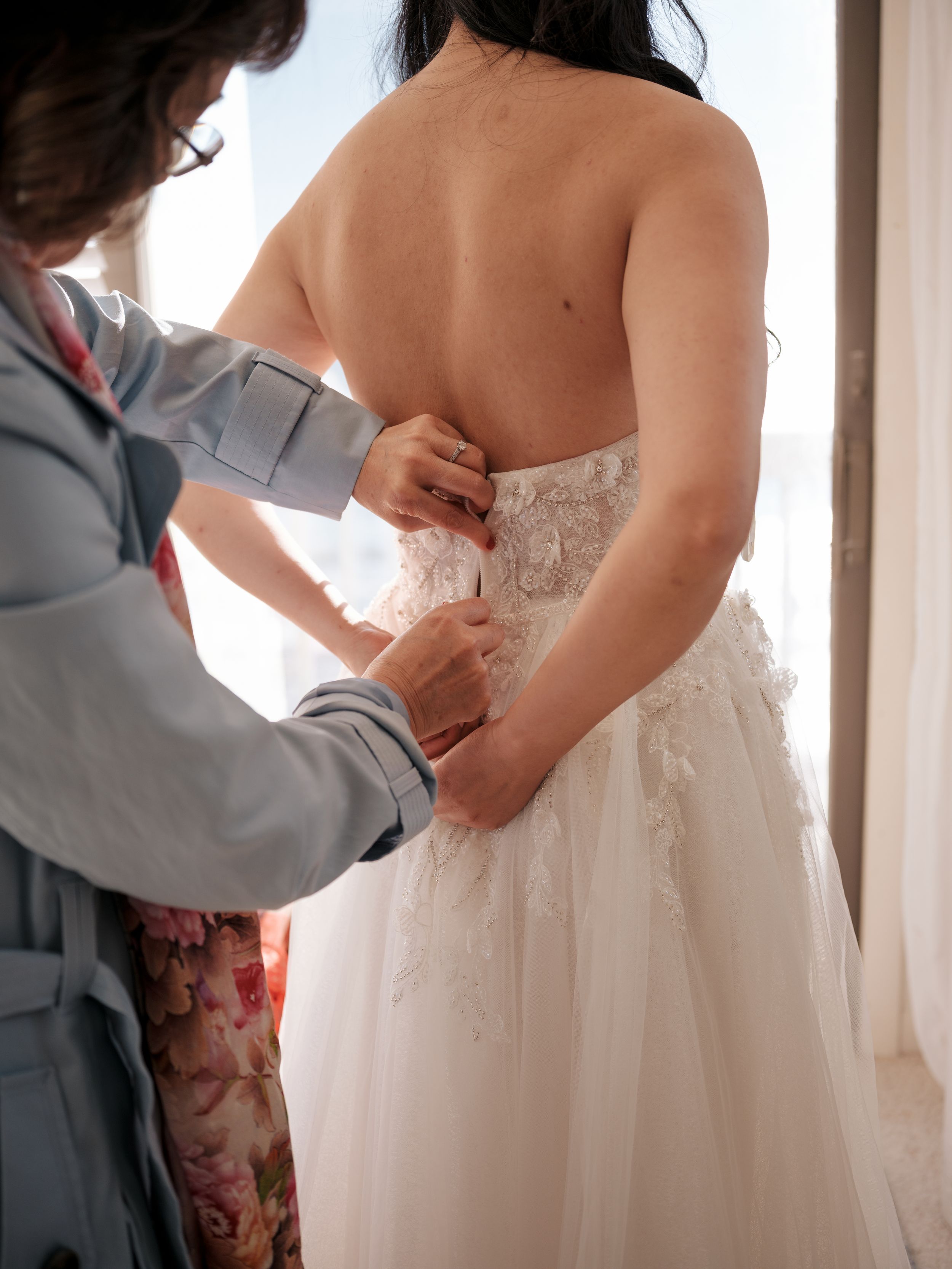 Helping hands adjusting the back of an elegant white wedding dress.
