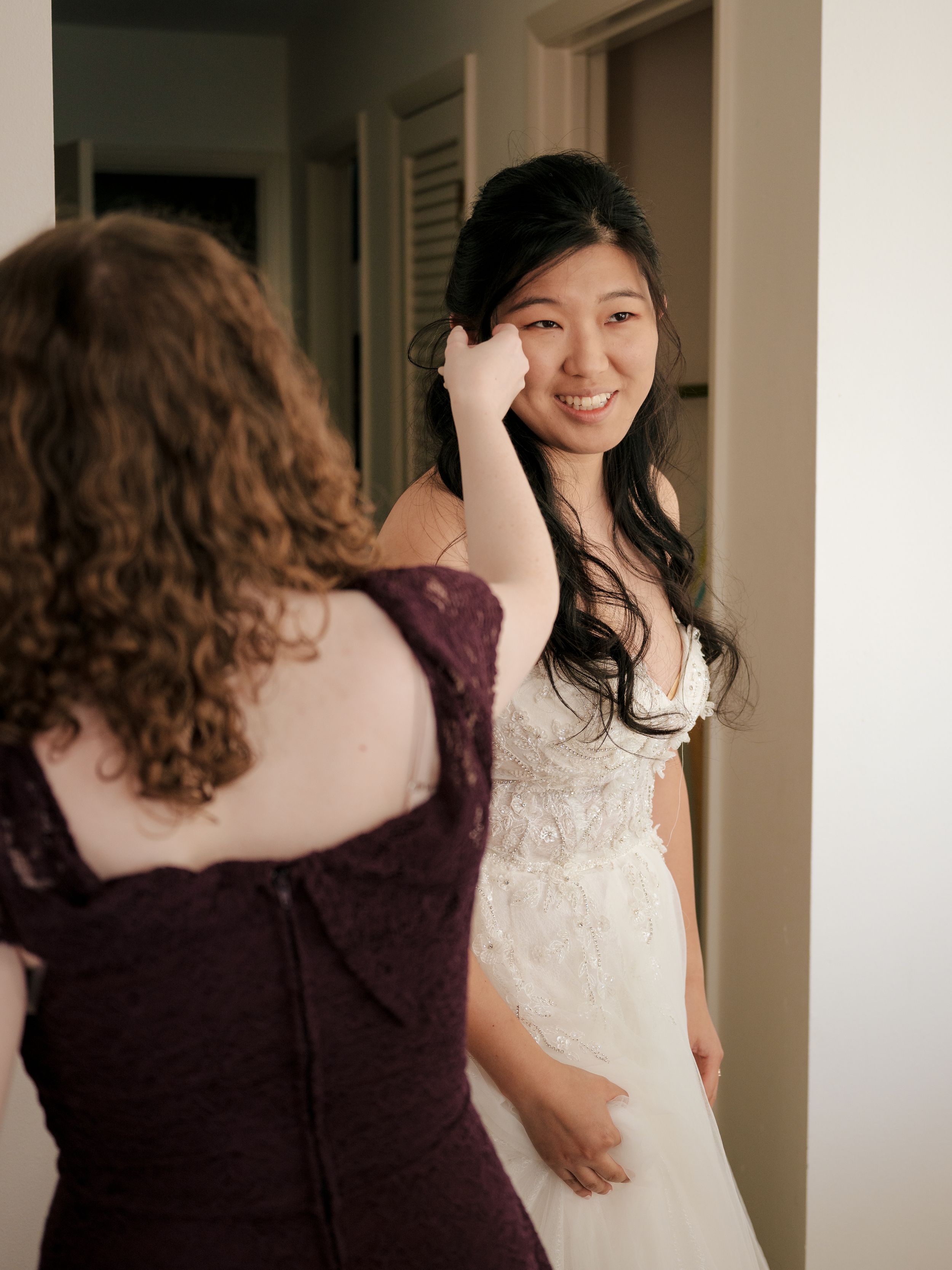 Two figures share a tender hug in a sunlit room, one wearing white and one in dark purple dress.