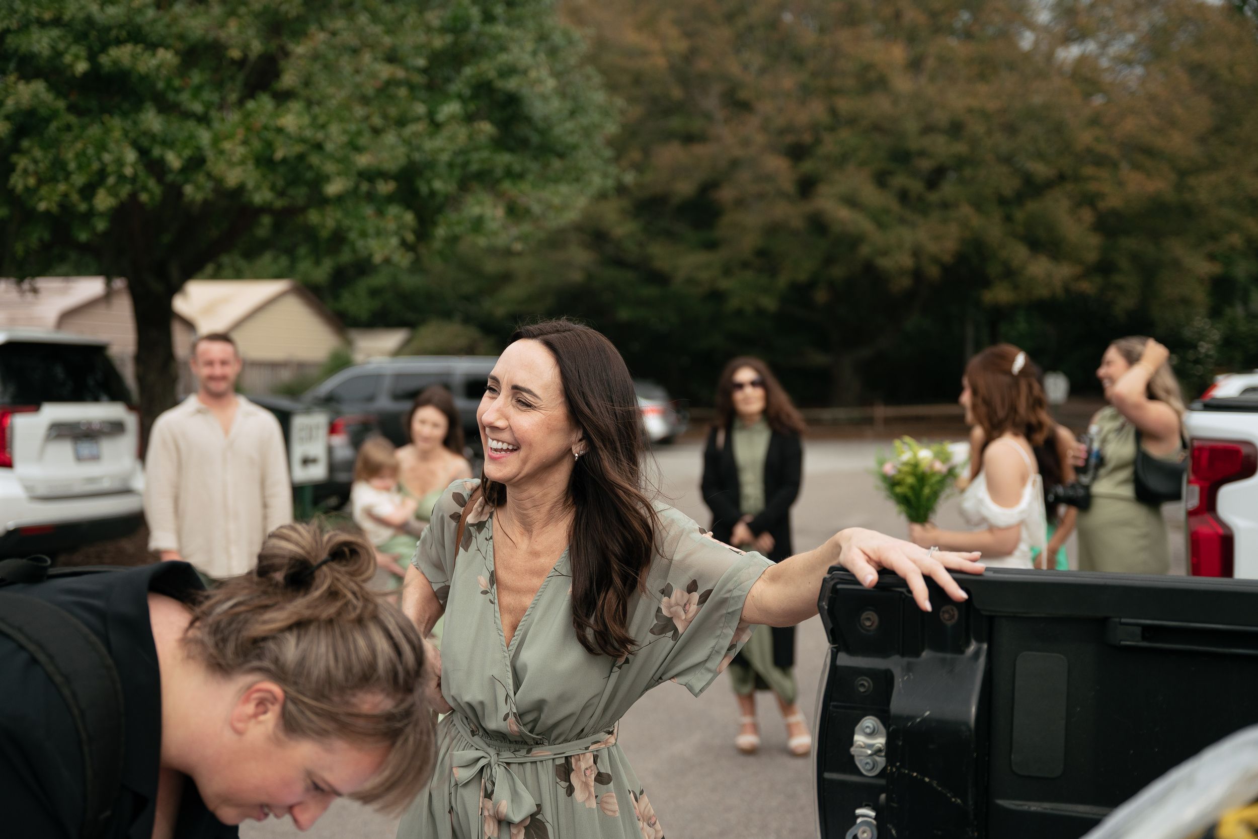 A joyful moment captured at an outdoor gathering with people interacting near parked cars.