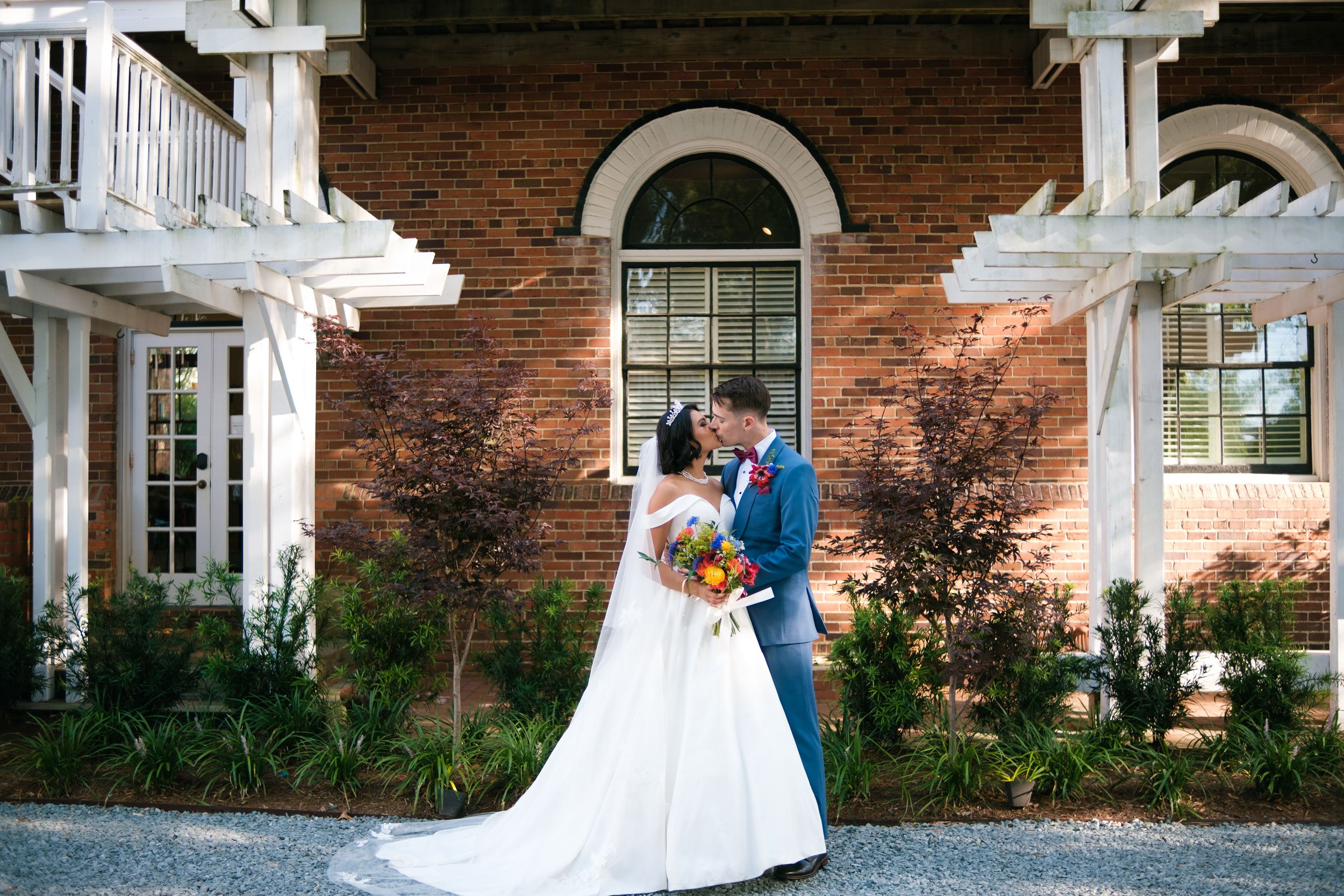 A couple poses romantically at various locations around a brick mansion with white columns and architectural details.