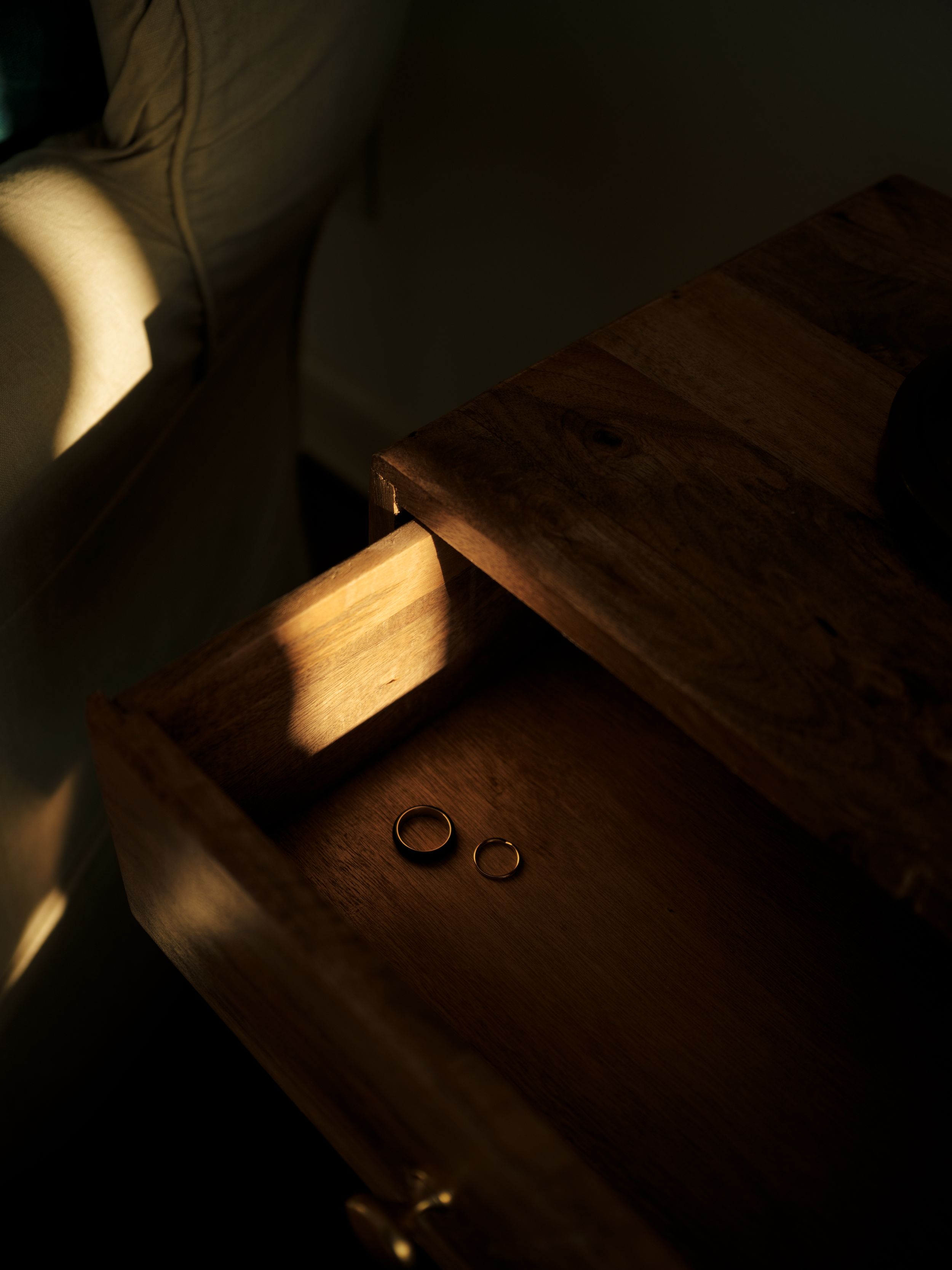 Wedding rings dramatically lit in shadows and natural light on a wooden surface.