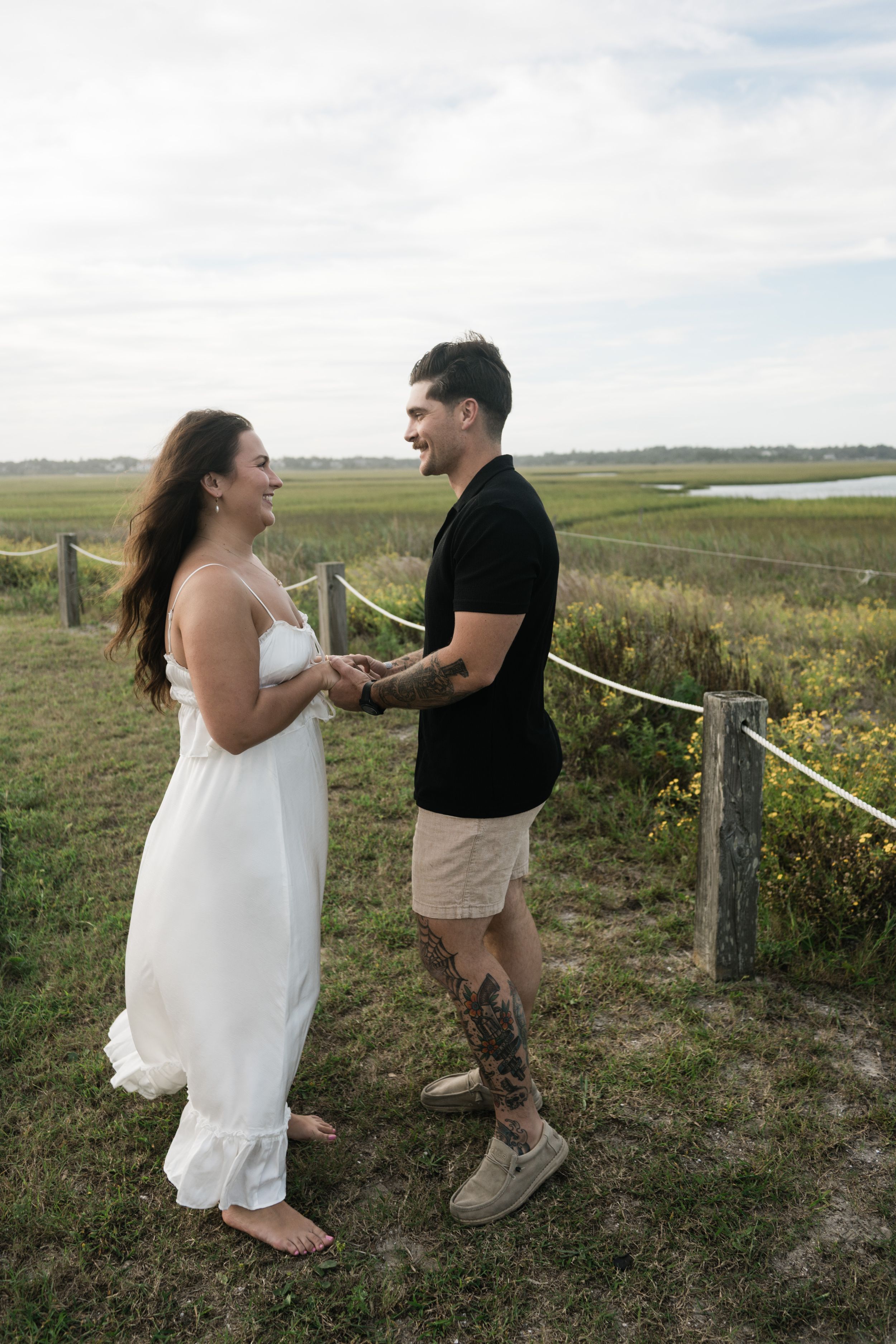 A couple shares a joyful moment together in a scenic field with rolling hills and wildflowers in the background.