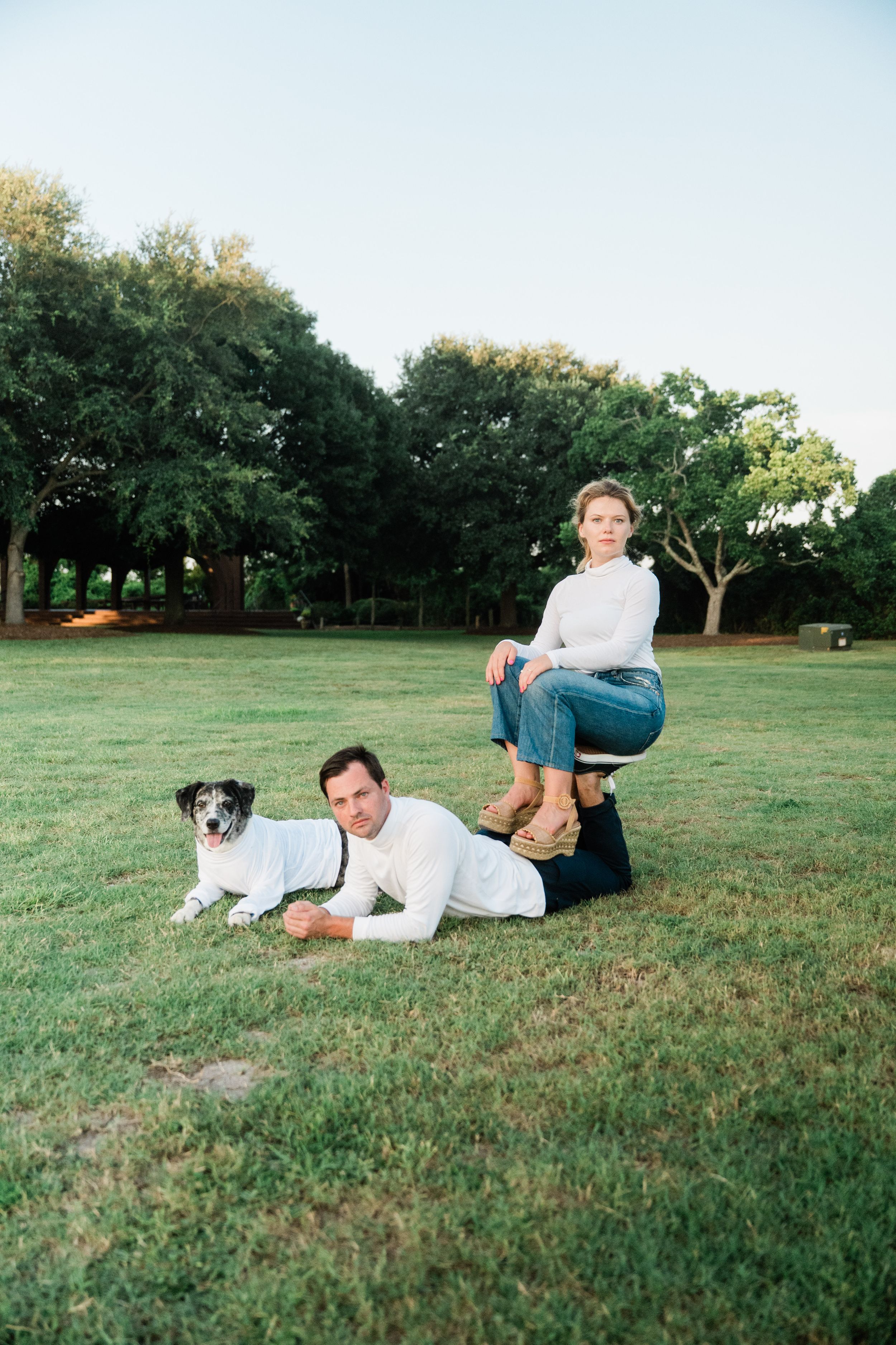 Person lying in grass with a dog while enjoying a sunny day outdoors in a park setting.
