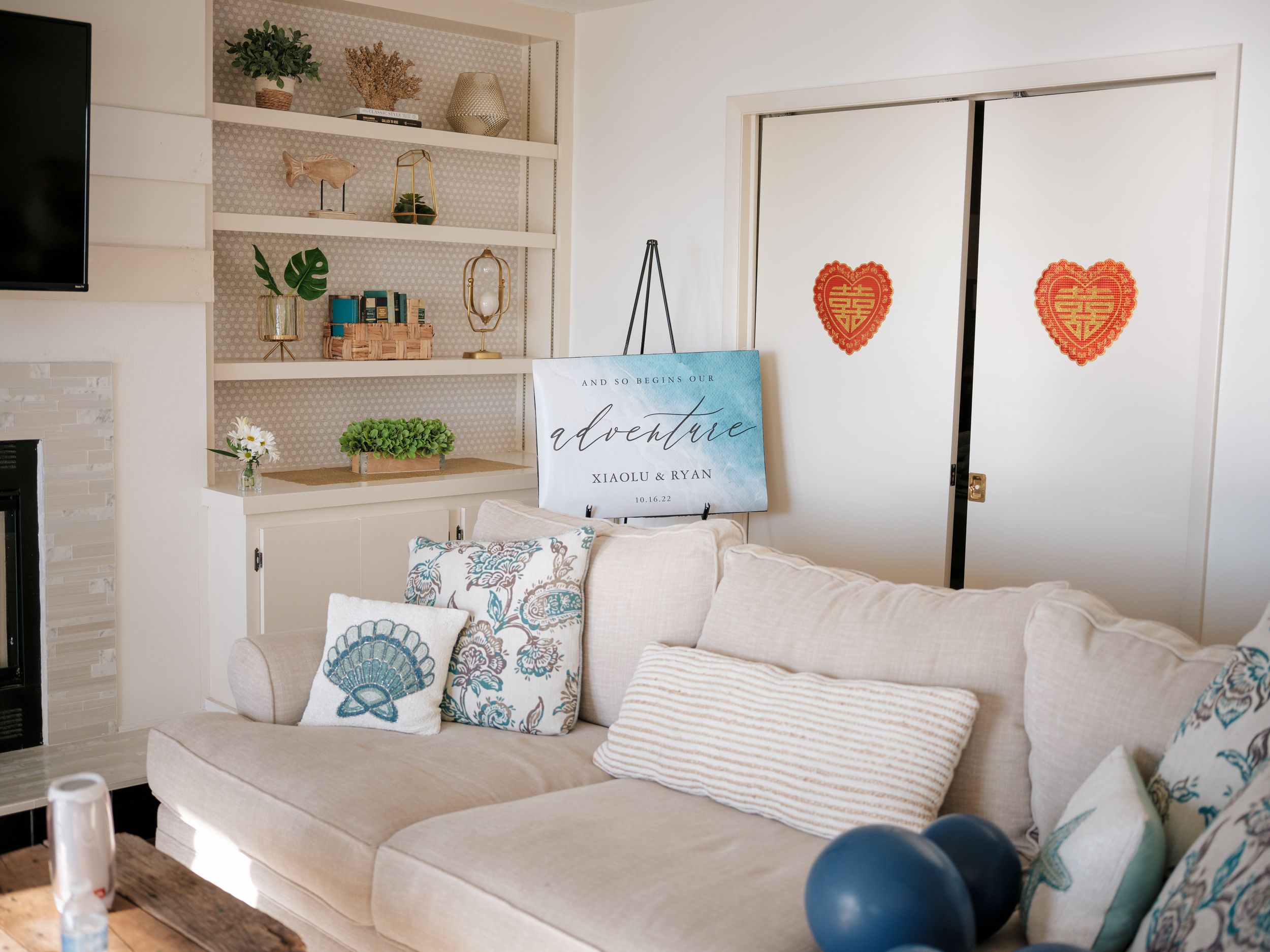 A modern white bedroom showcases built-in shelving, heart-shaped wall decor, and coastal-inspired throw pillows.