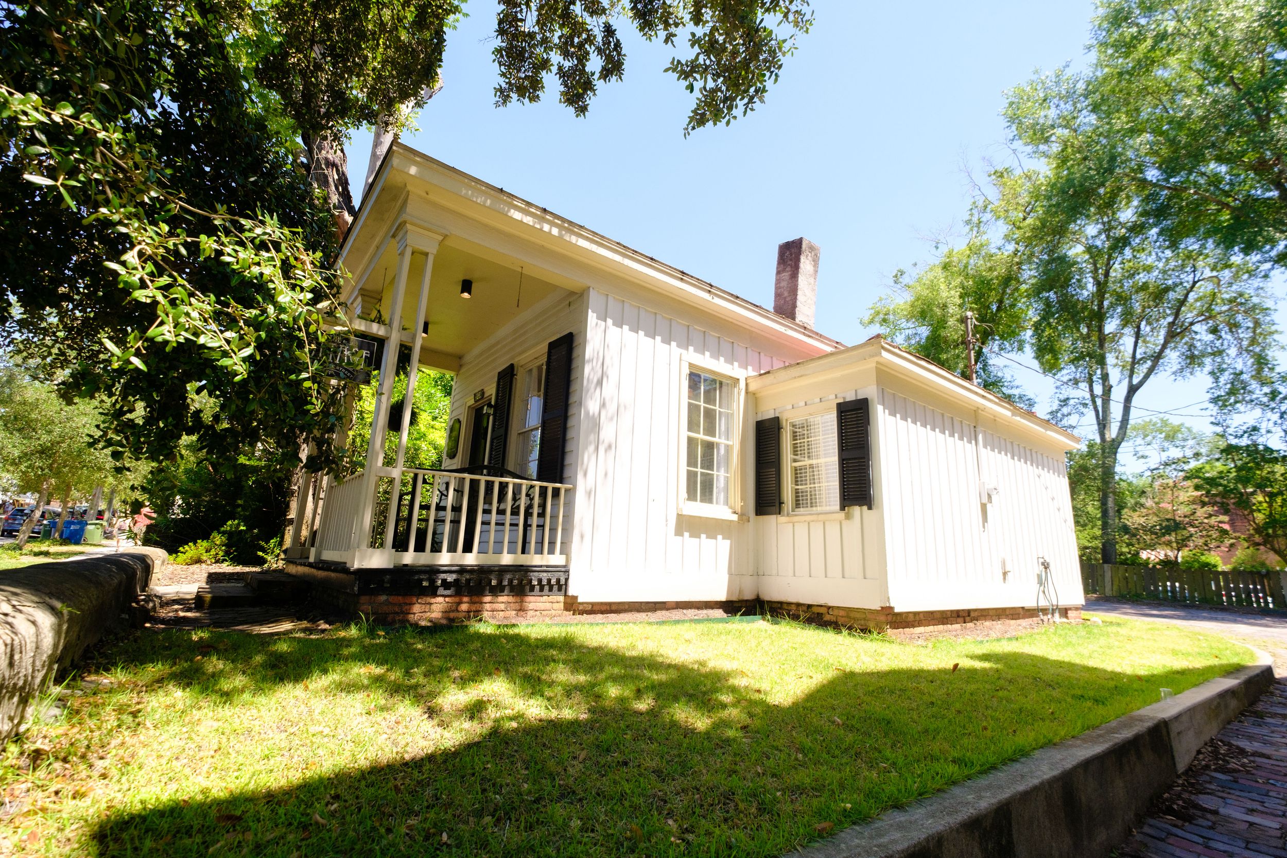 Wide panoramic view of a white residential house with green lawn and mature trees in the backyard.