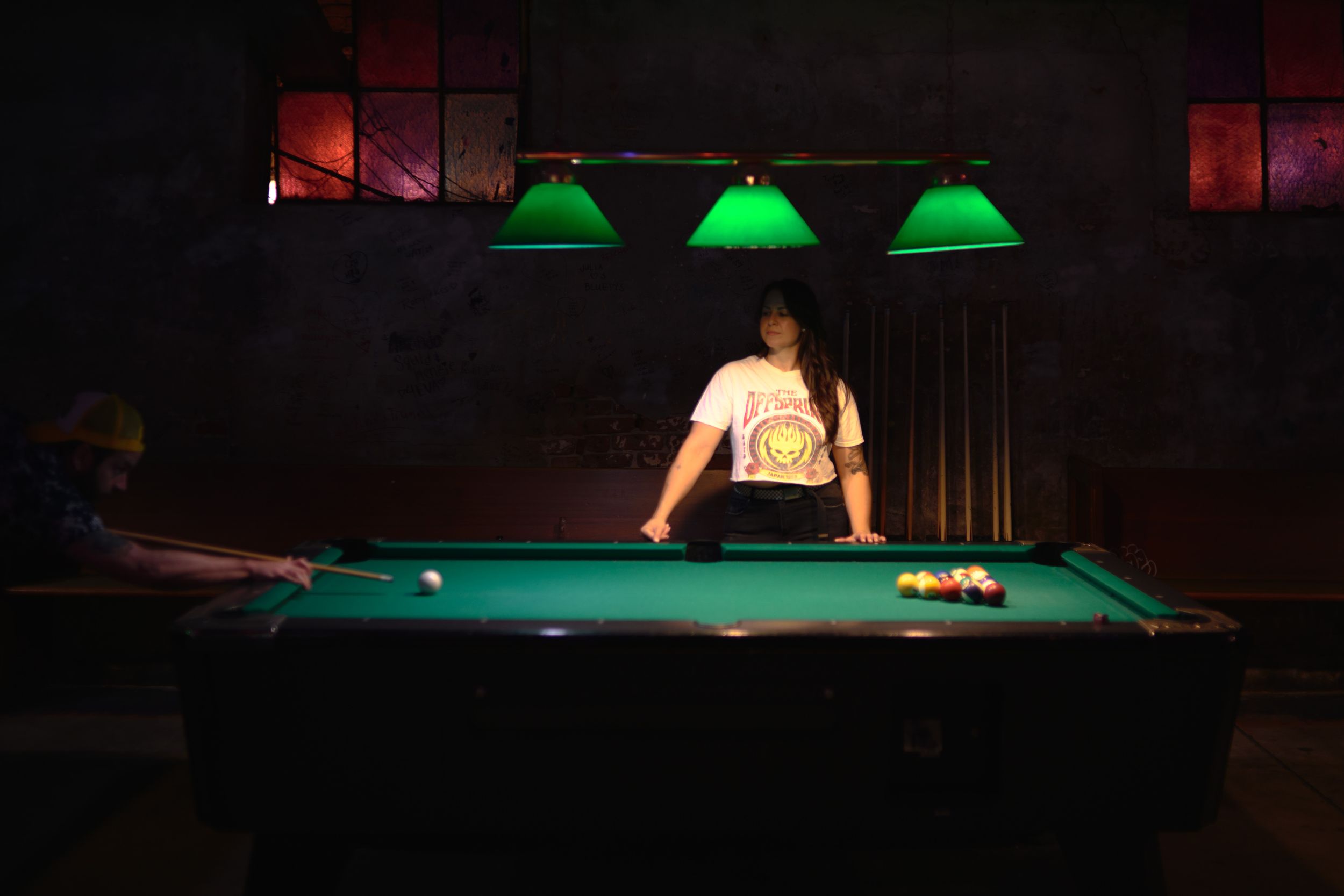 Green-lit pool table in a dark bar setting with ambient lighting.