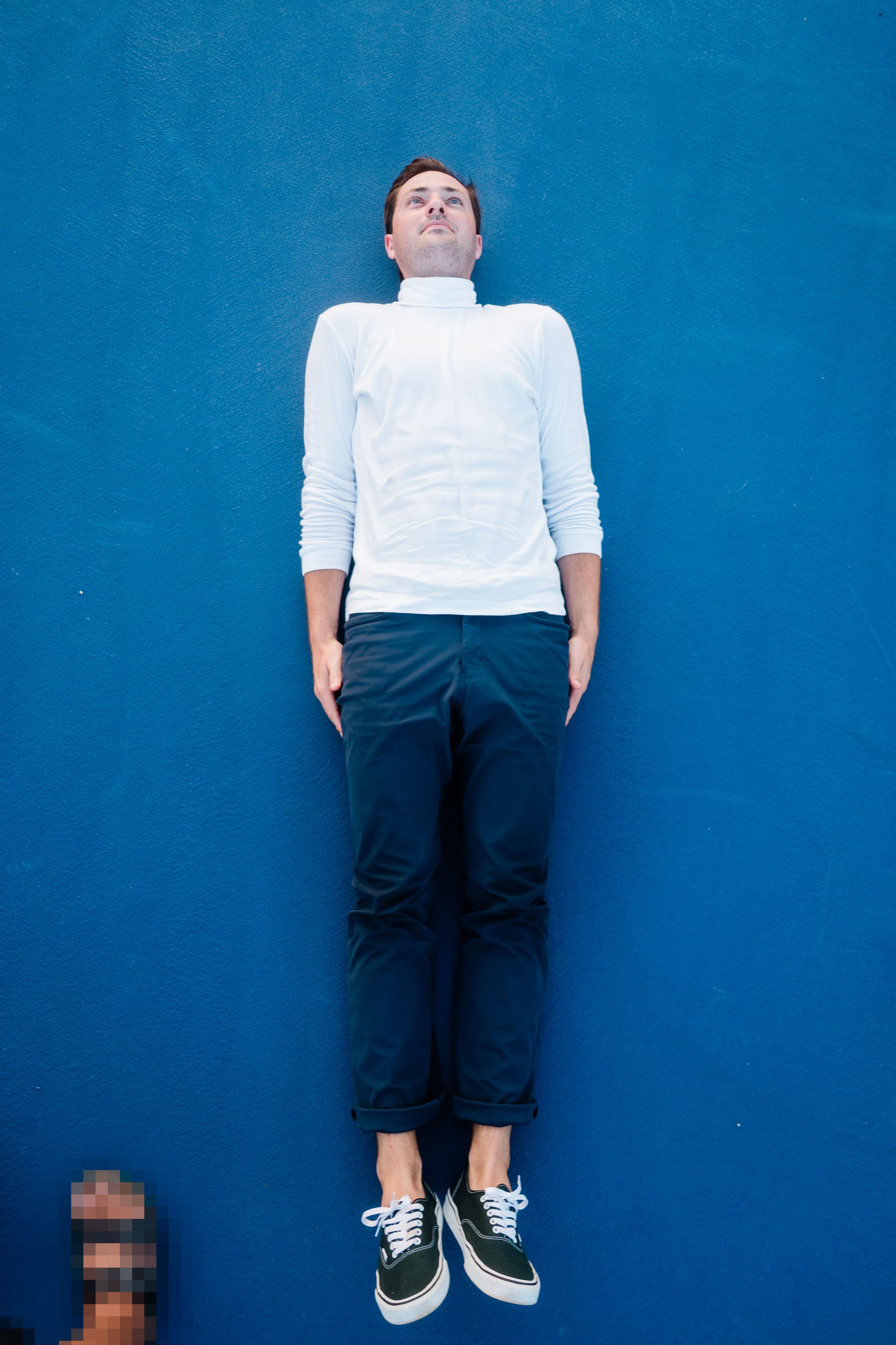 Person wearing white shirt and dark pants lying on blue background viewed from different angles.