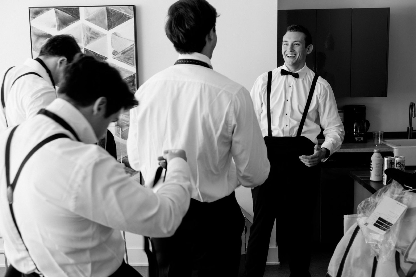 Black and white photo of groomsmen getting ready in formal attire with suspenders.