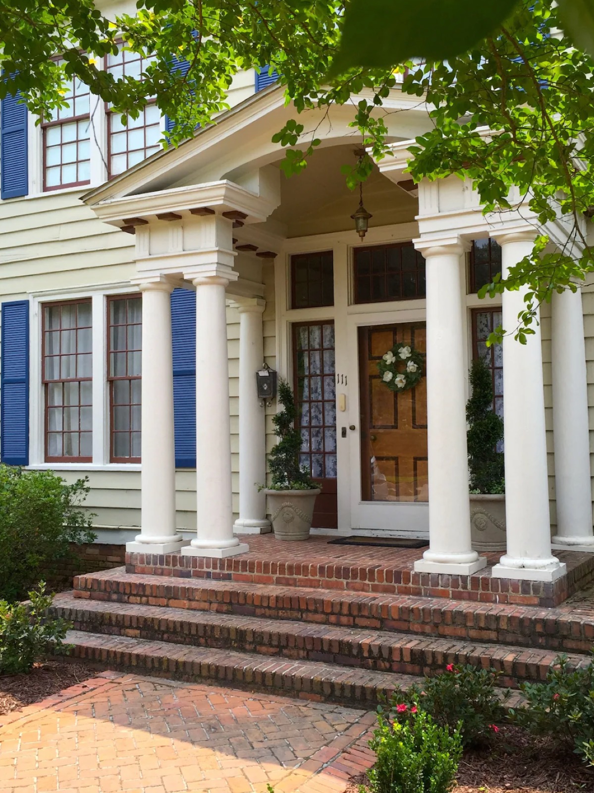 Classic colonial home entrance with white columns, blue shutters, and brick steps.