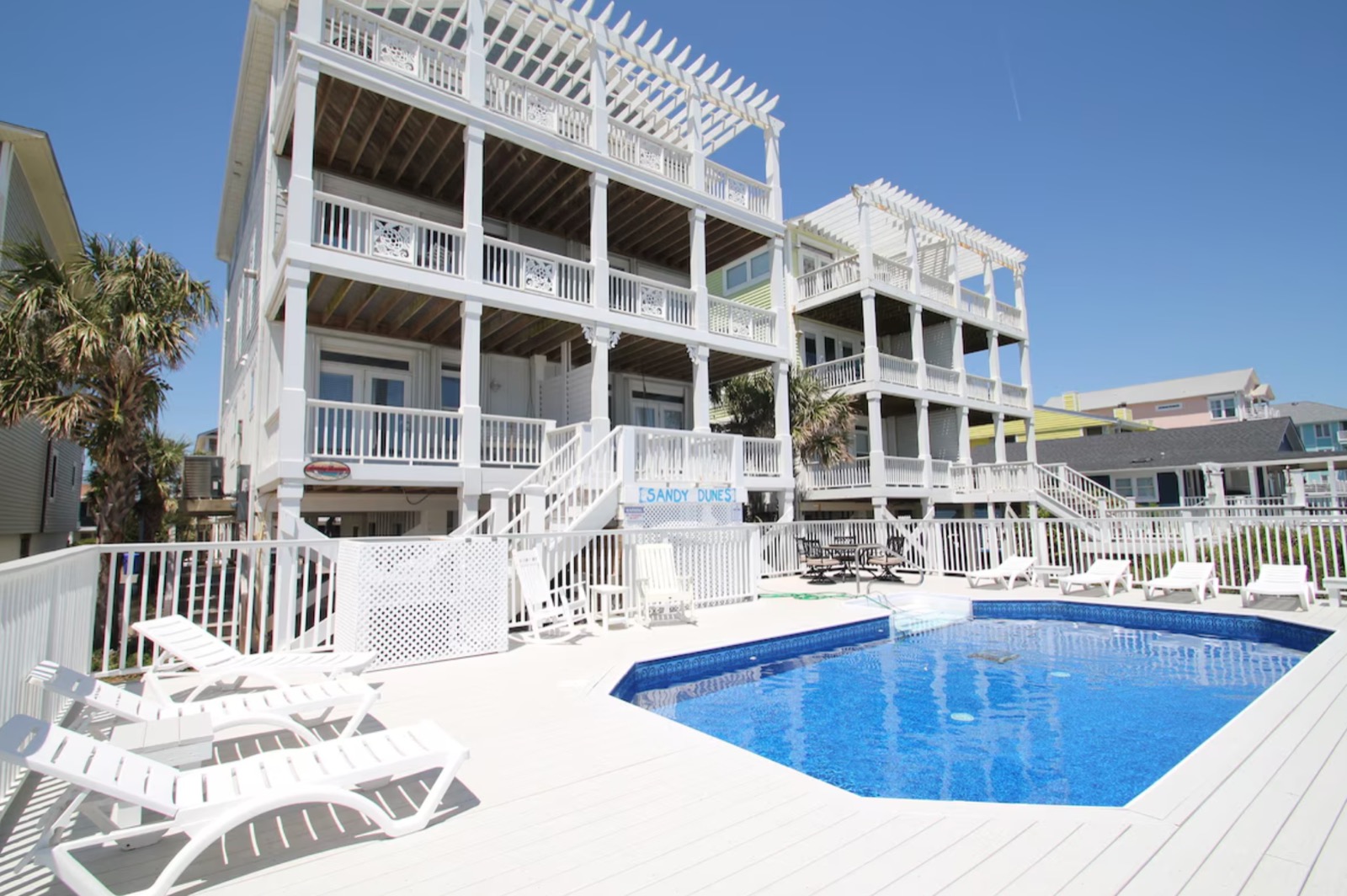 White beach house with multiple balconies and pergolas overlooking a swimming pool.