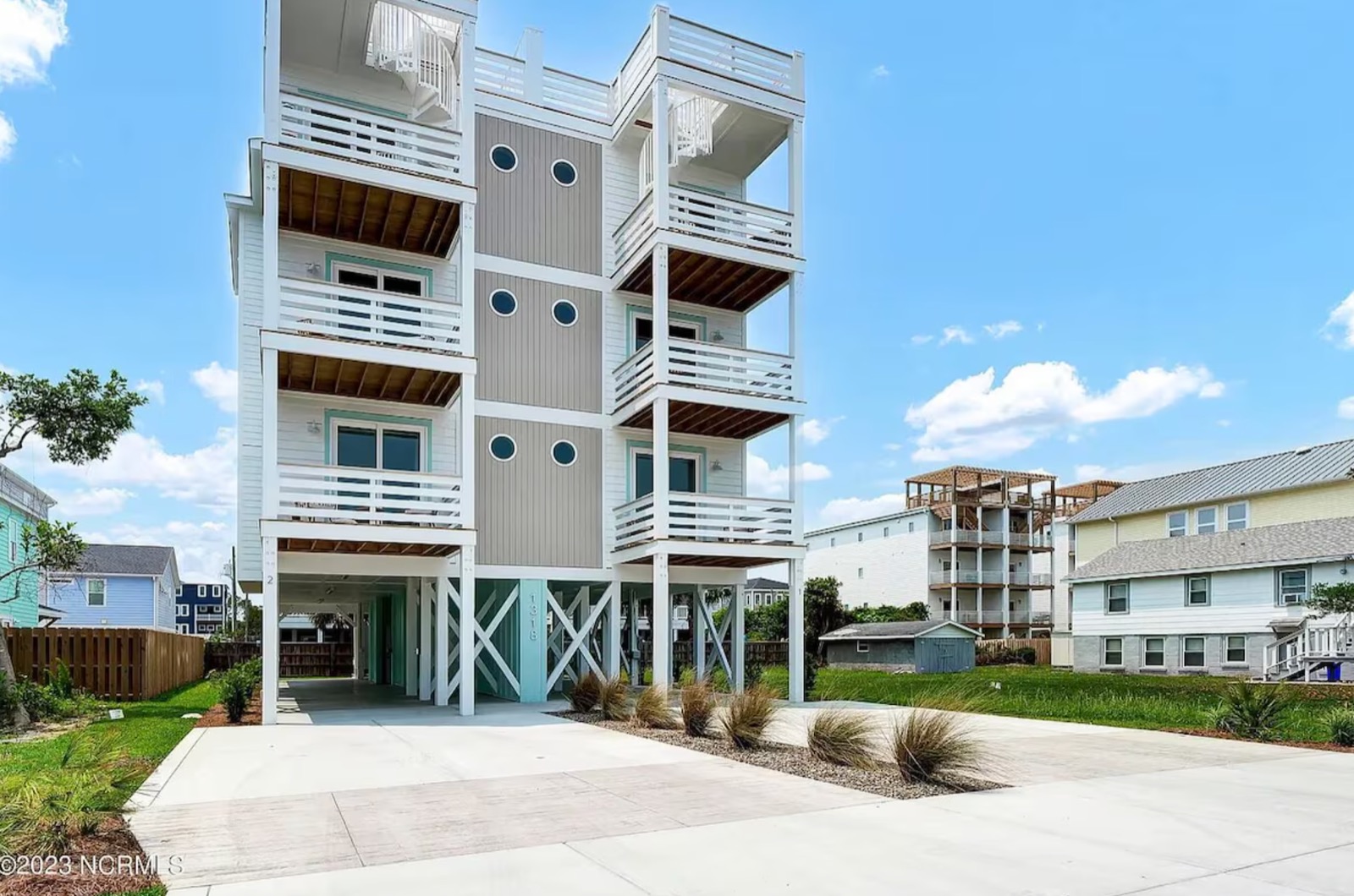 Modern three-story beach house with white exterior and multiple balconies supported by stilts.