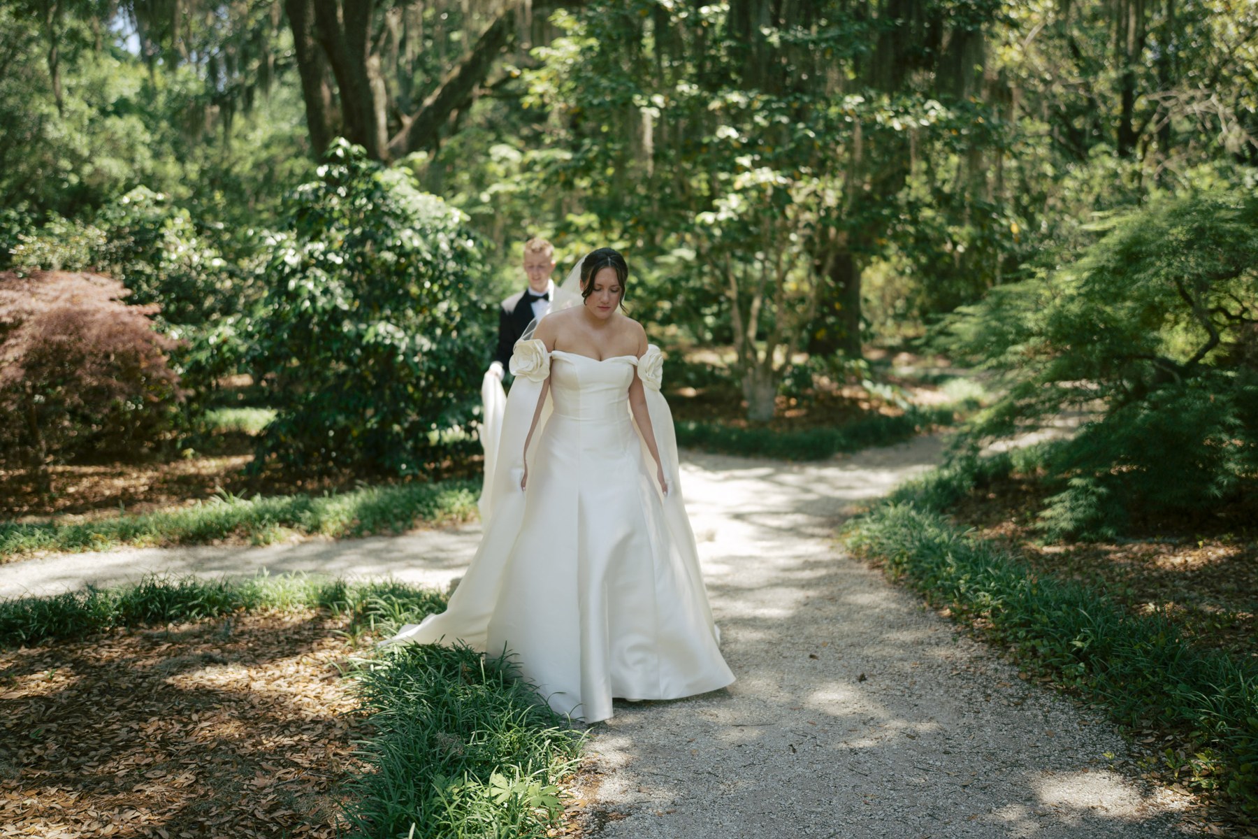 Lizzy standing alone in her wedding dress on a tree lined garden path