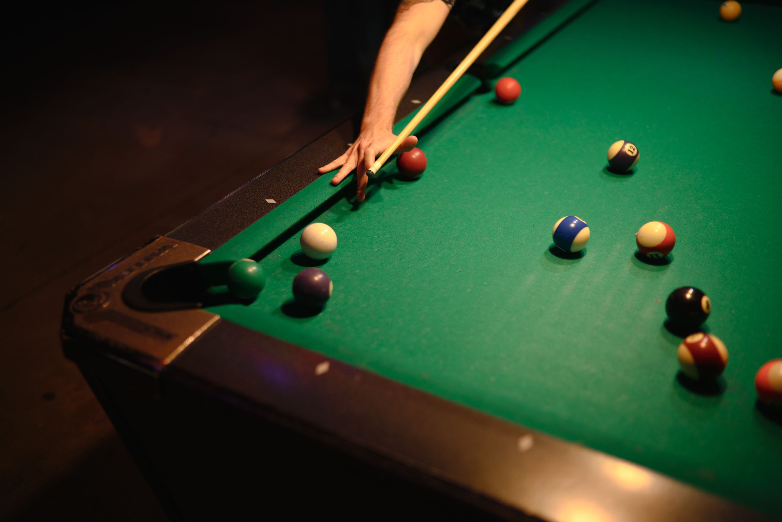 Close-up shot of a pool table with scattered billiard balls on green felt under dramatic lighting.