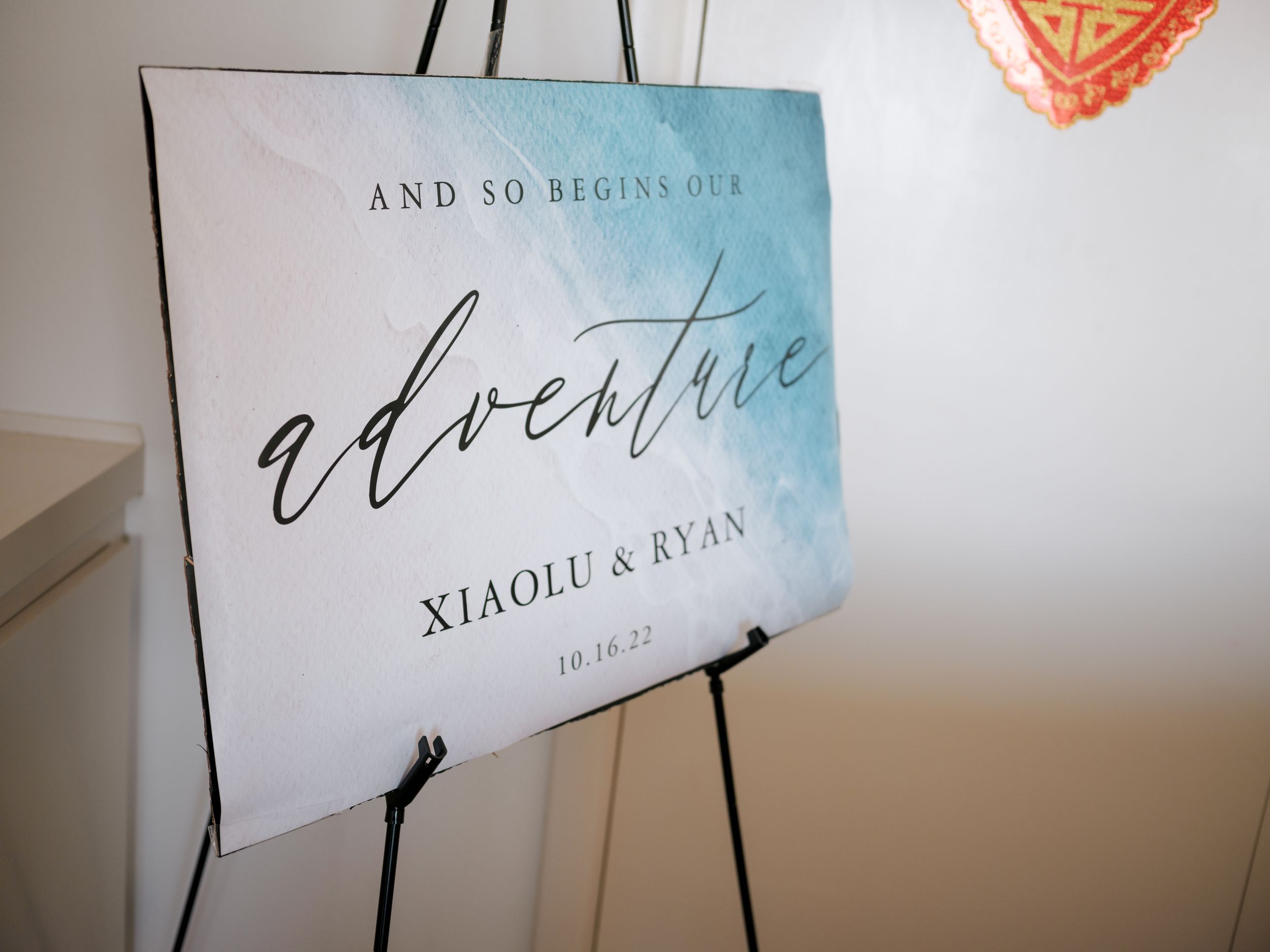 Decorative wedding sign in elegant calligraphy displayed on a white easel during a celebration.