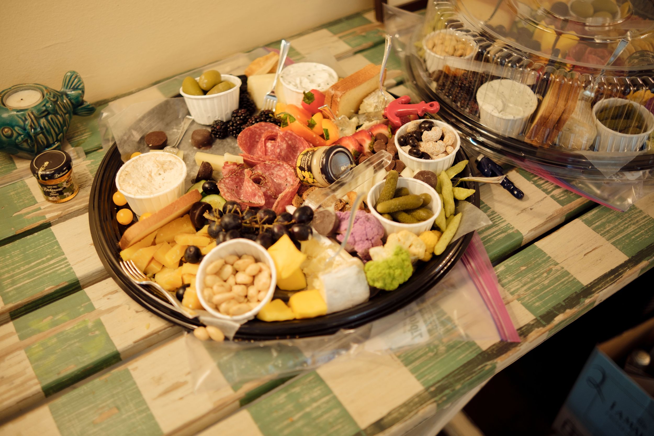 A long table covered with various appetizers, cheese plates, wine bottles and small plates on a checkered tablecloth.