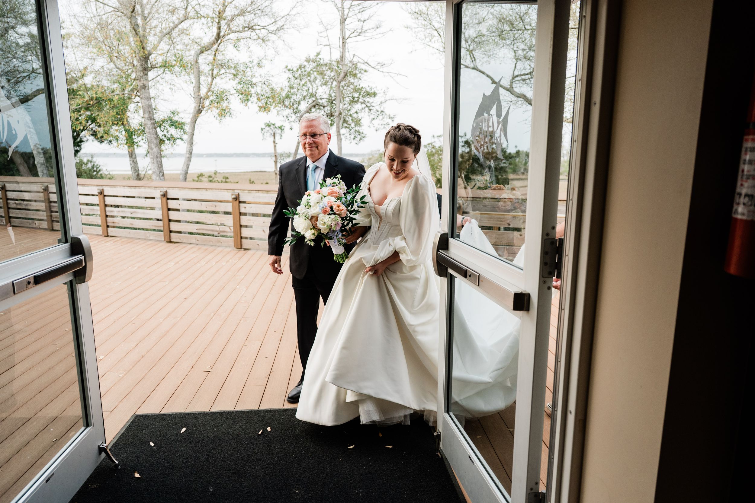 Wedding party enters through doorway onto wooden deck overlooking scenic view.
