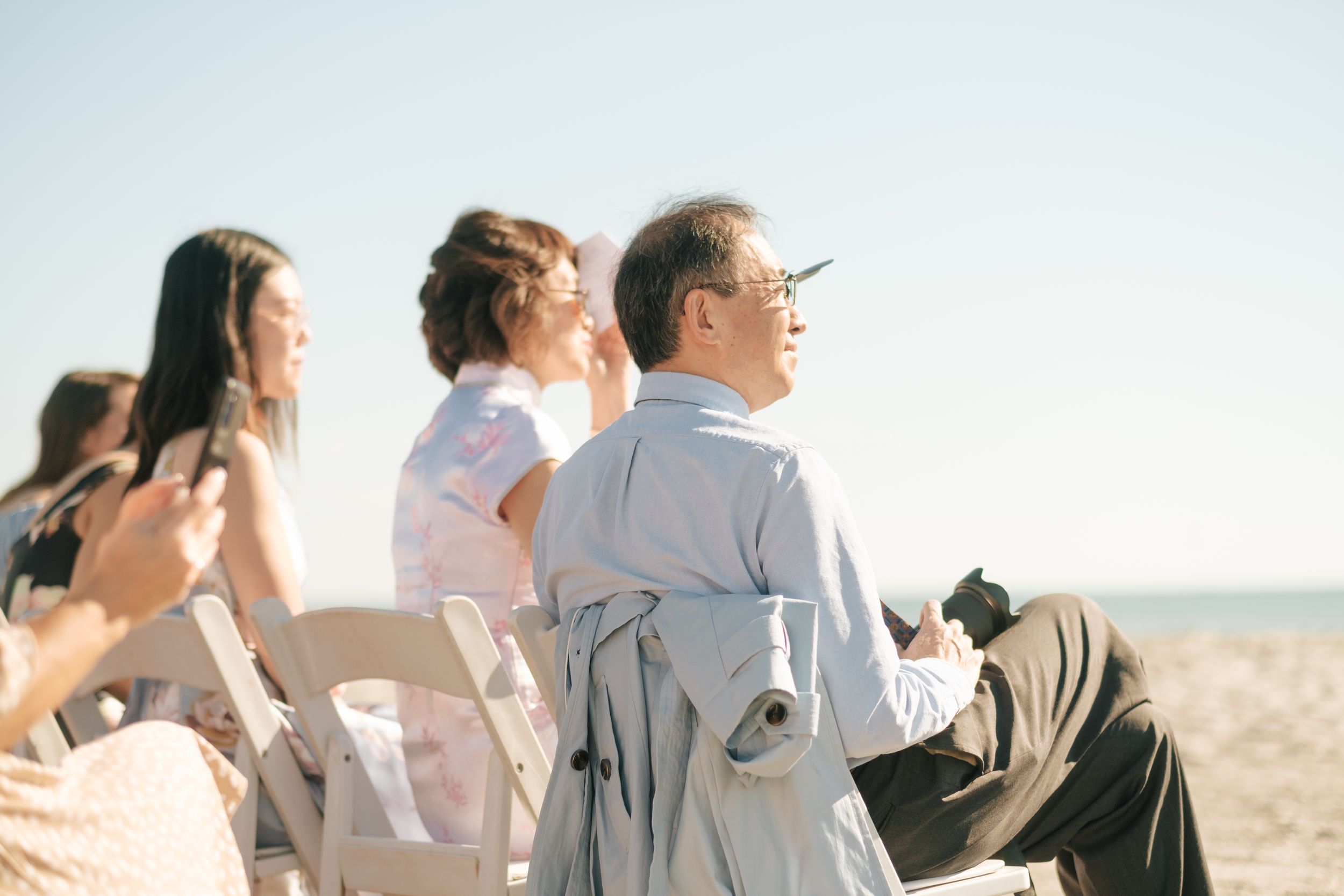 Guests watching a beach wedding ceremony under clear blue skies.