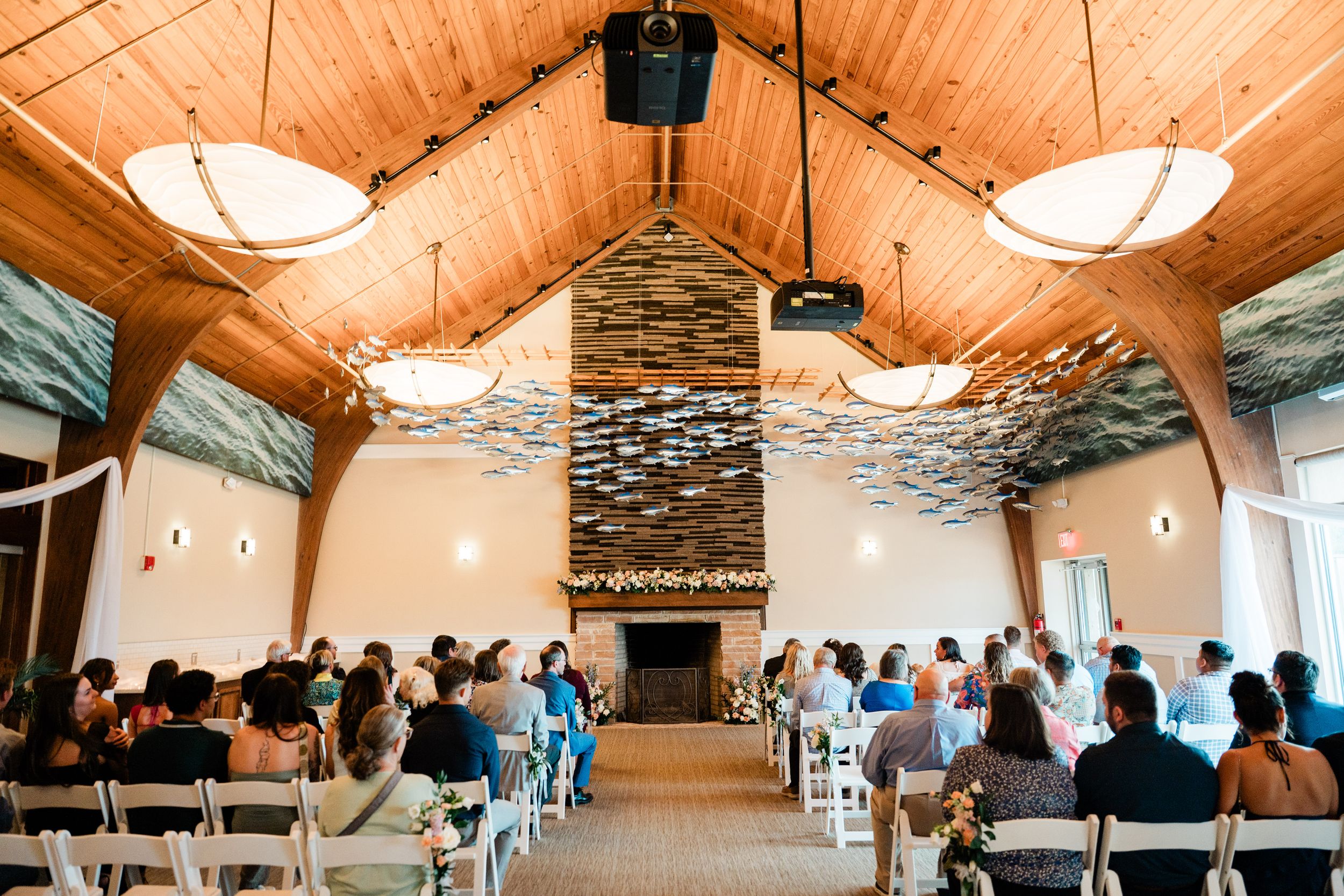 Wedding ceremony venue interior with vaulted wood ceiling, stone fireplace and rows of guest seating.