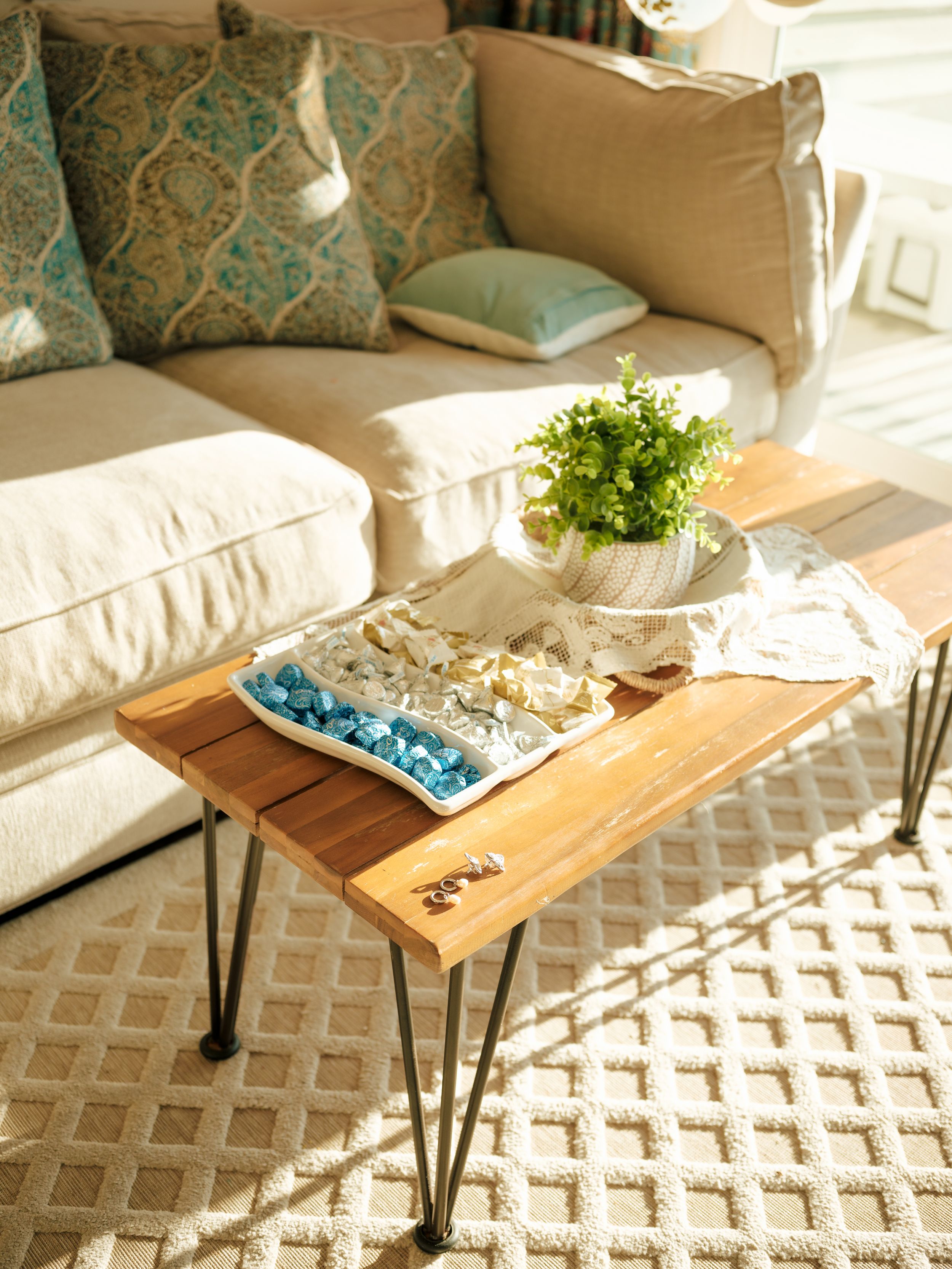 Modern coffee table with hairpin legs styled with decor items on a geometric rug beside a cream sofa with teal pillows.