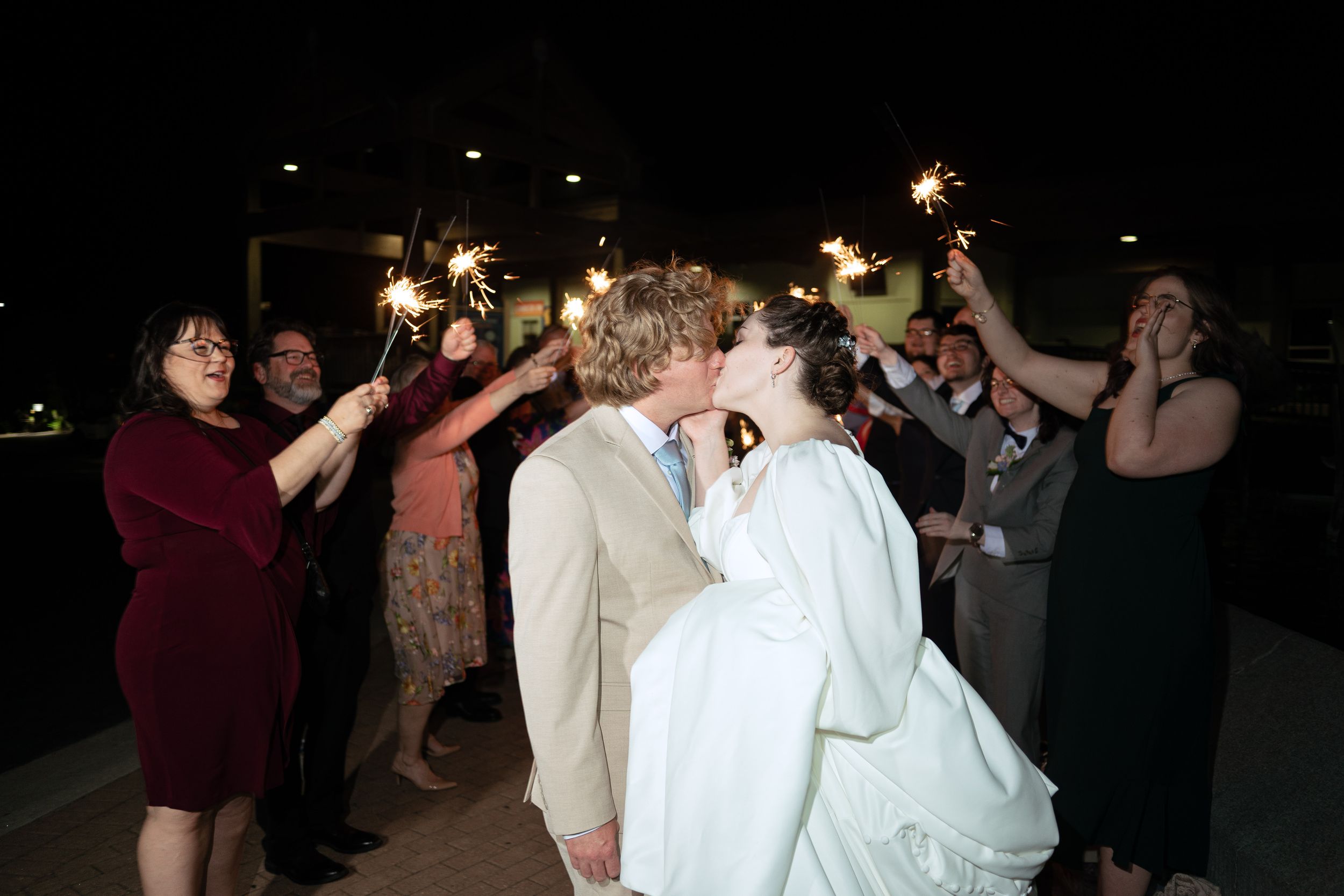 Wedding guests hold sparklers during a nighttime send-off celebration.