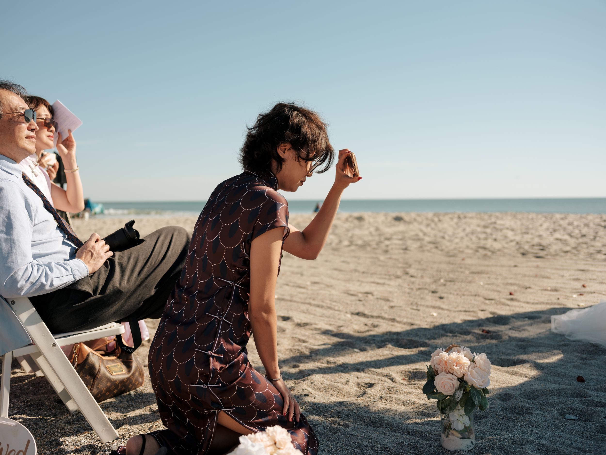 Beach wedding scene with guests photographing the ceremony.