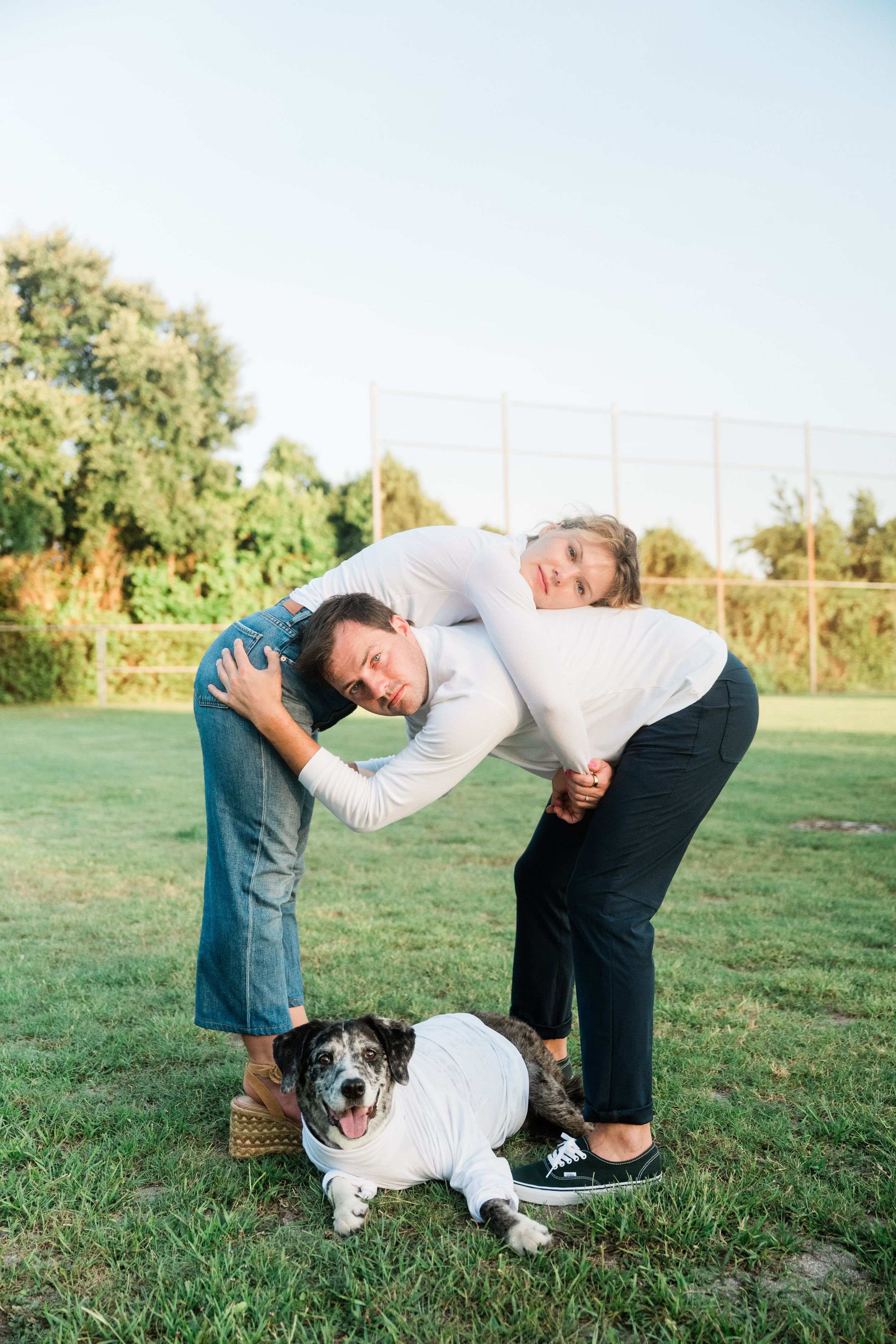 A person in a white sweater bends down to pet a black and white dog on green grass in a sunny outdoor setting.